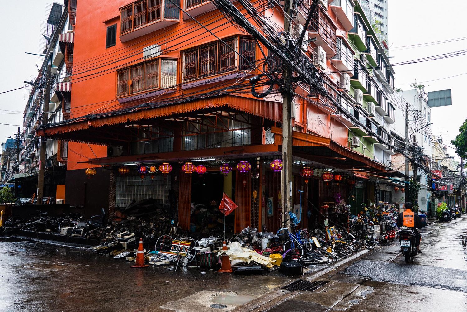 Motorcycles parked outside an orange corner building on a rainy street in an Asian city.