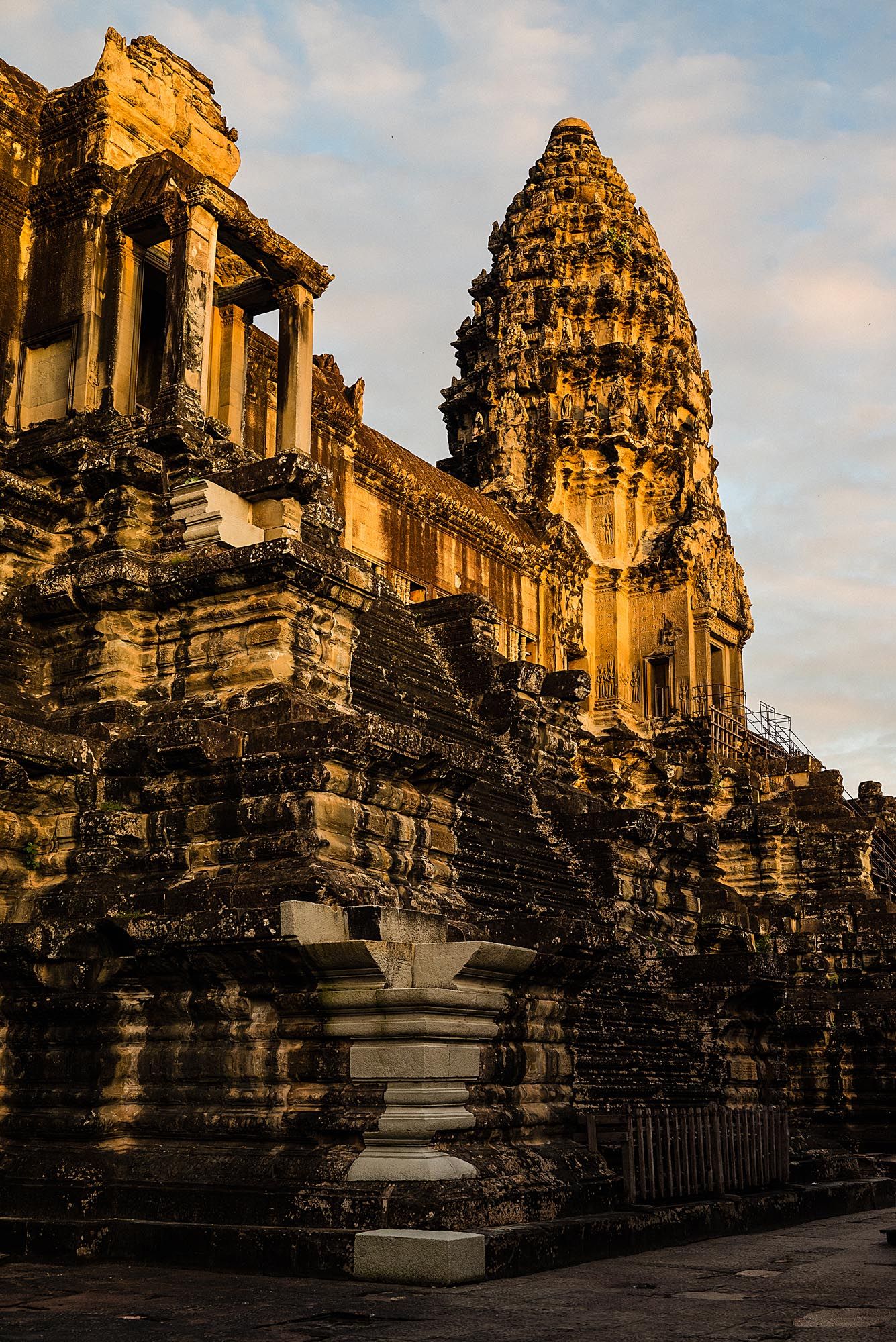 Ancient stone towers and structures of Angkor Wat temple complex illuminated by warm golden sunlight at sunset.