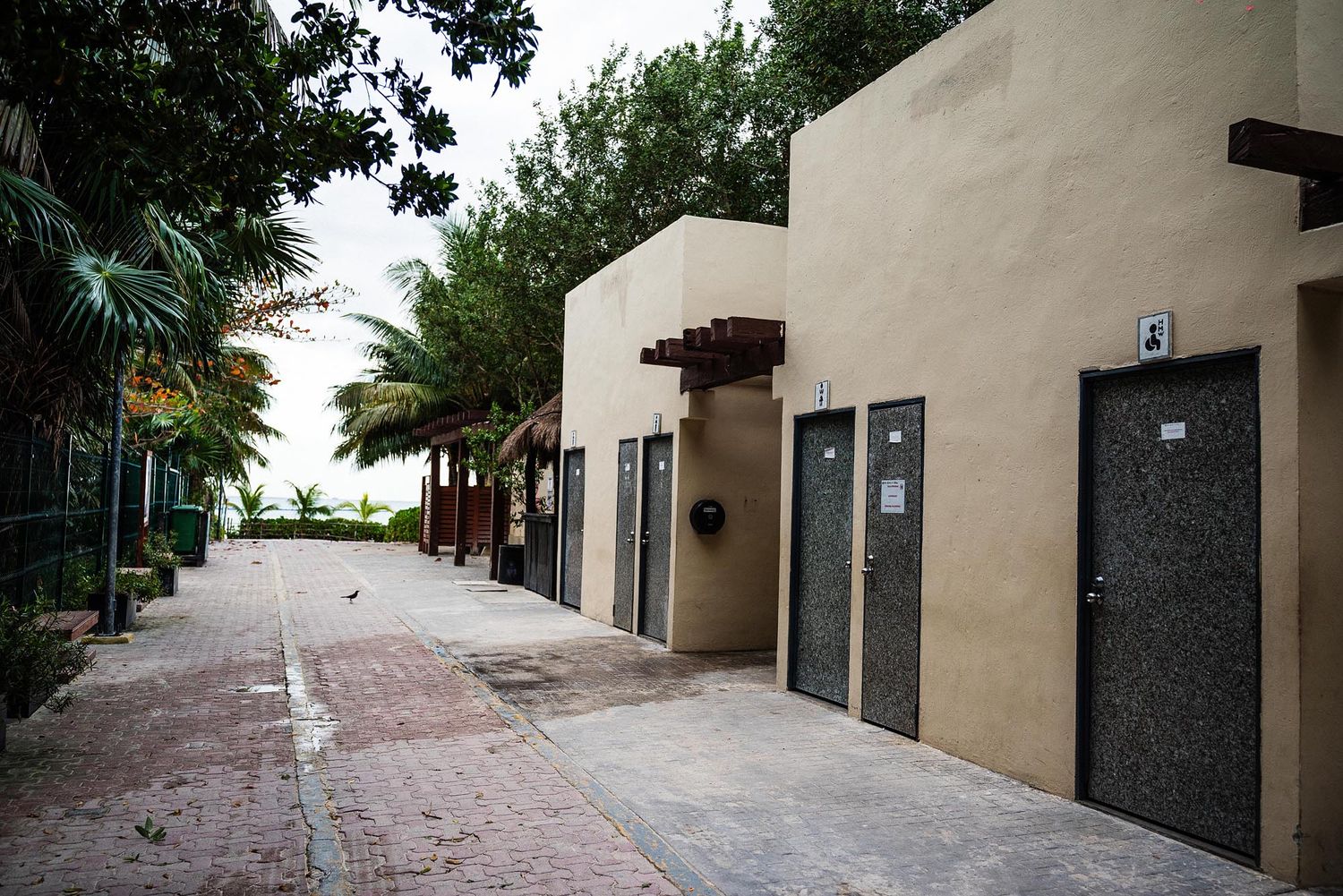A long brick-paved walkway extends between beige stucco buildings with palm trees and landscaping along the path.