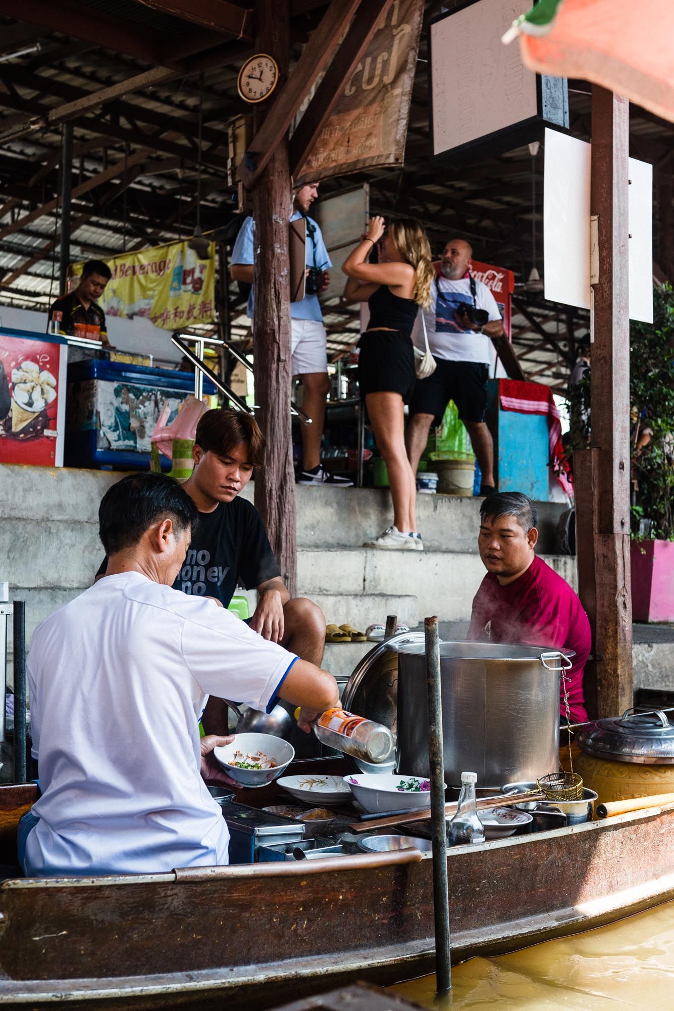 Vendors prepare and serve food at a rustic outdoor market stall with wooden beams and counter space.