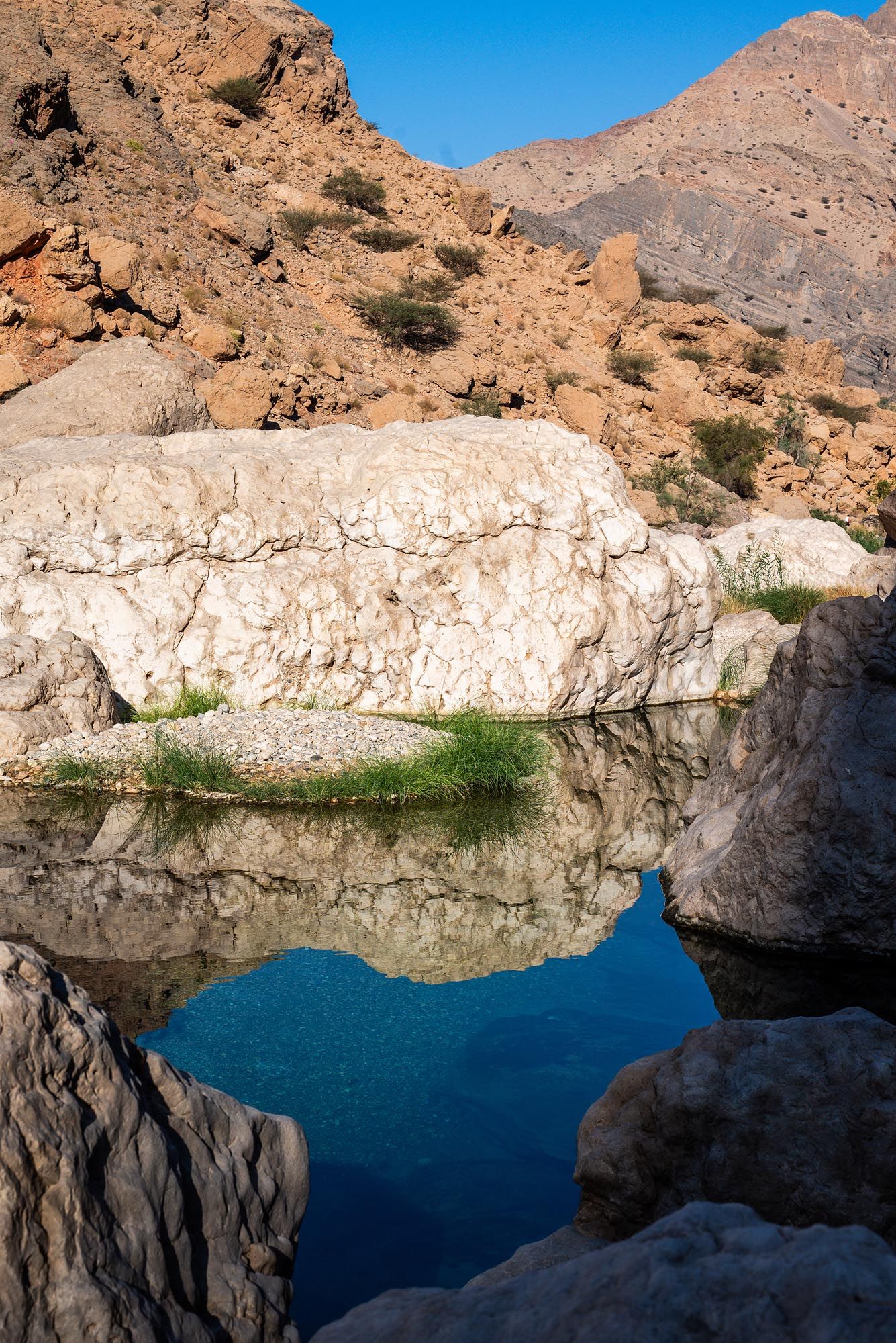 Scenic desert oasis with crystal blue water reflecting white limestone cliffs and rugged mountains in Oman. Wadi Al Arbeieen