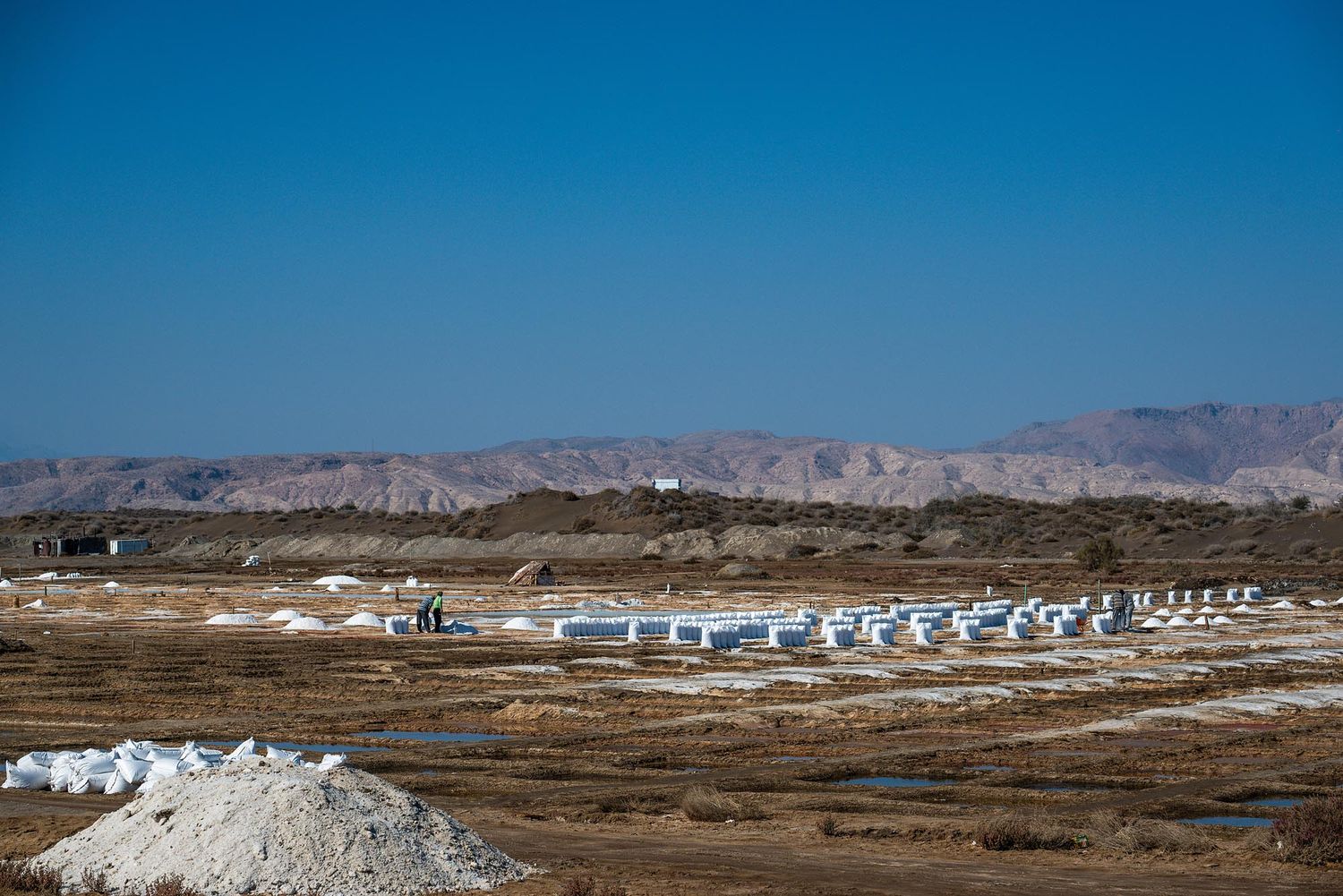 A panoramic view of white storage tanks and industrial facilities in an arid desert landscape with mountains in the background.