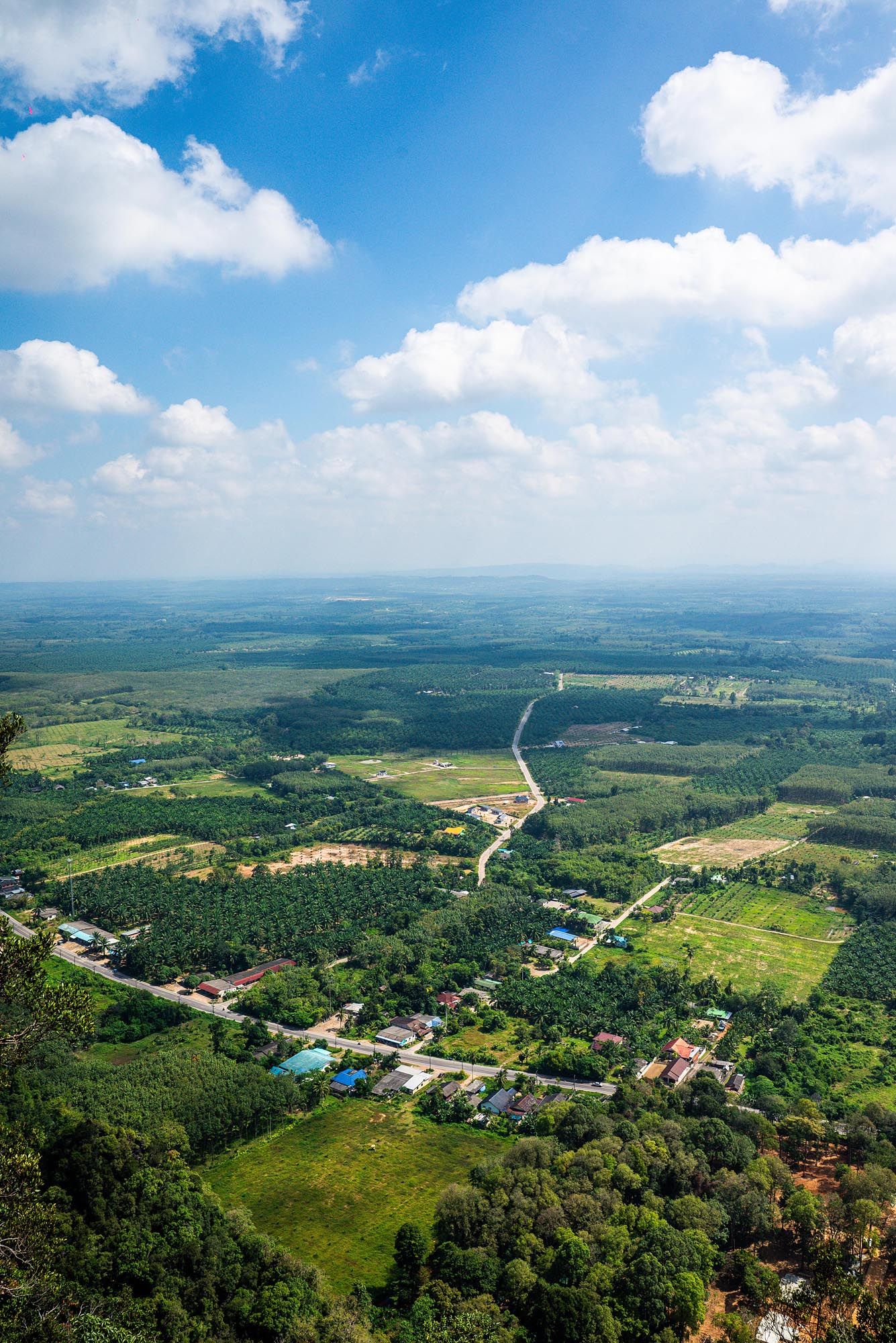 Aerial panoramic view of a rural landscape with winding roads, green fields, and scattered buildings under blue skies.