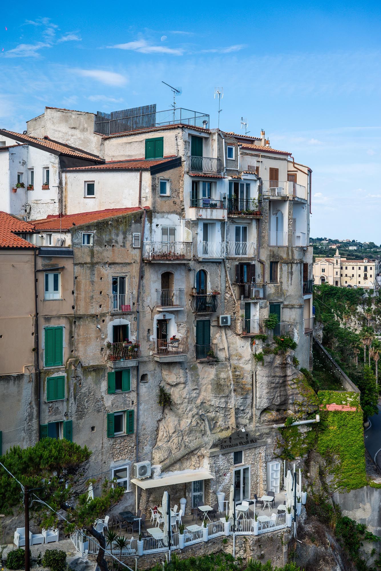 Historic cliff-side houses with green shutters and weathered stone walls perch precariously along the Italian coastline.