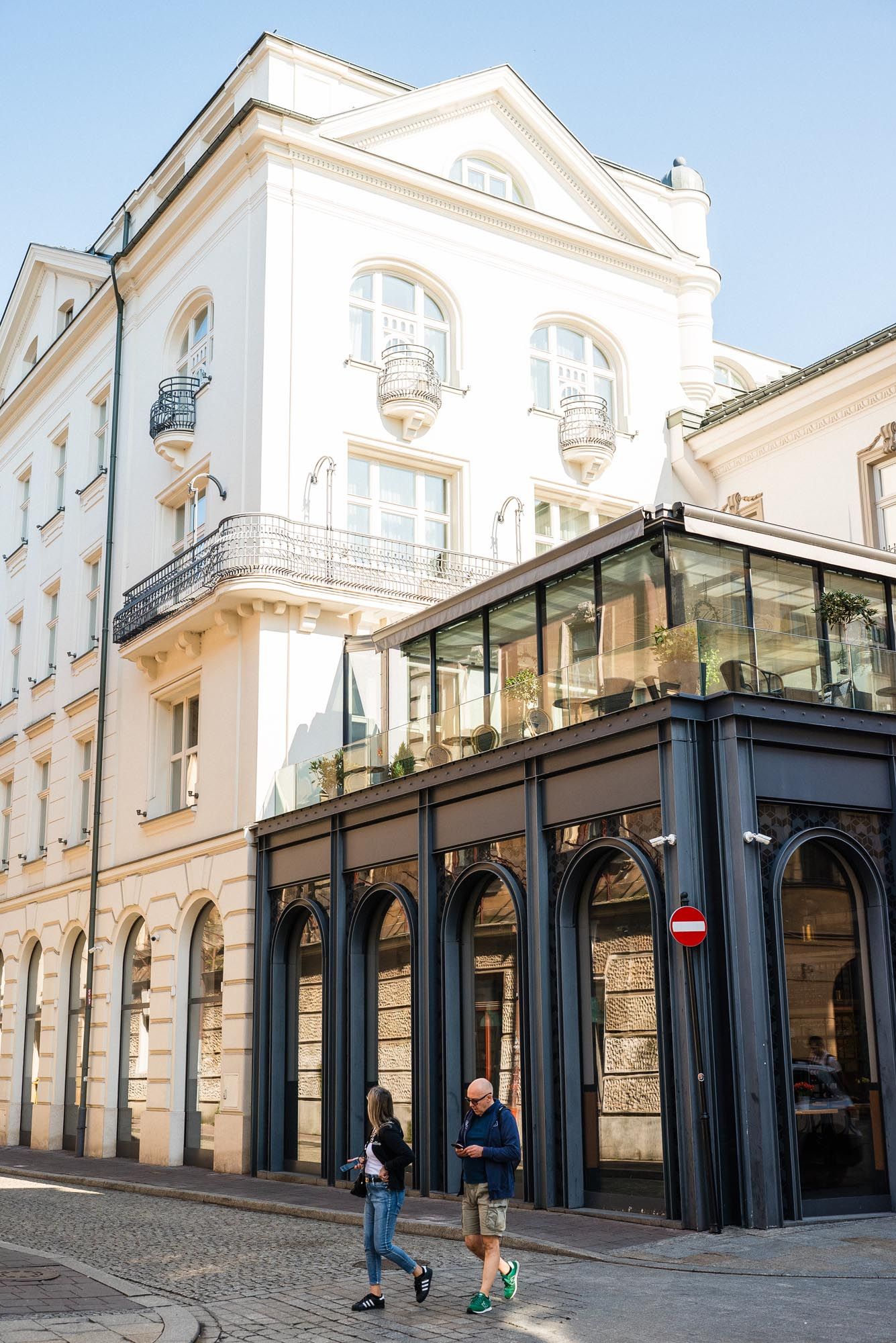 Historic white building with ornate balconies and black iron storefront in European city street corner with pedestrians walking.