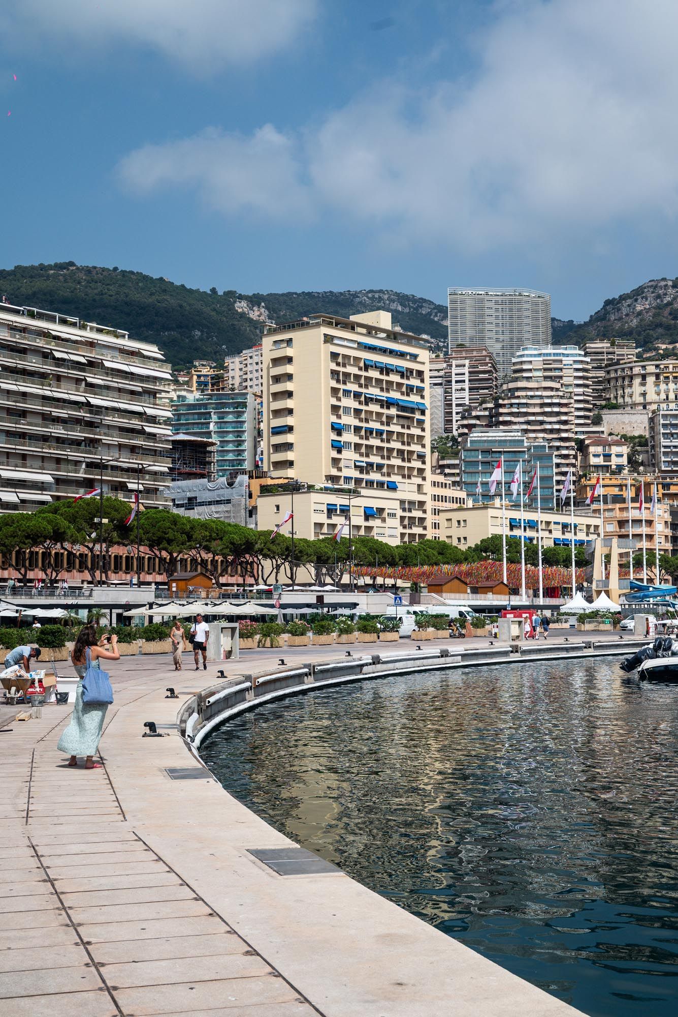 Panoramic view of a Mediterranean coastal promenade with modern apartment buildings and boats docked along the waterfront.