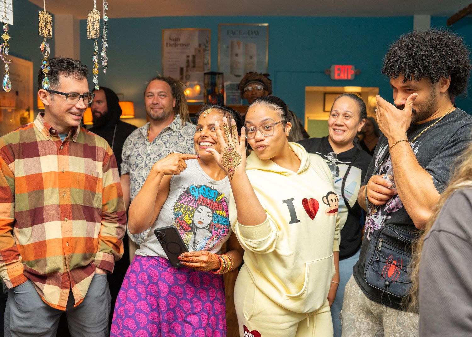 Group of joyful people celebrating an engagement at an indoor gathering, woman showing ring.