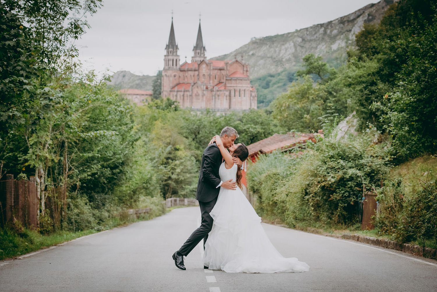Postboda en Covadonga, Asturias. Pareja de novios abrazándose en la carretera con la basílica al fondo, fotografía documental sin poses.