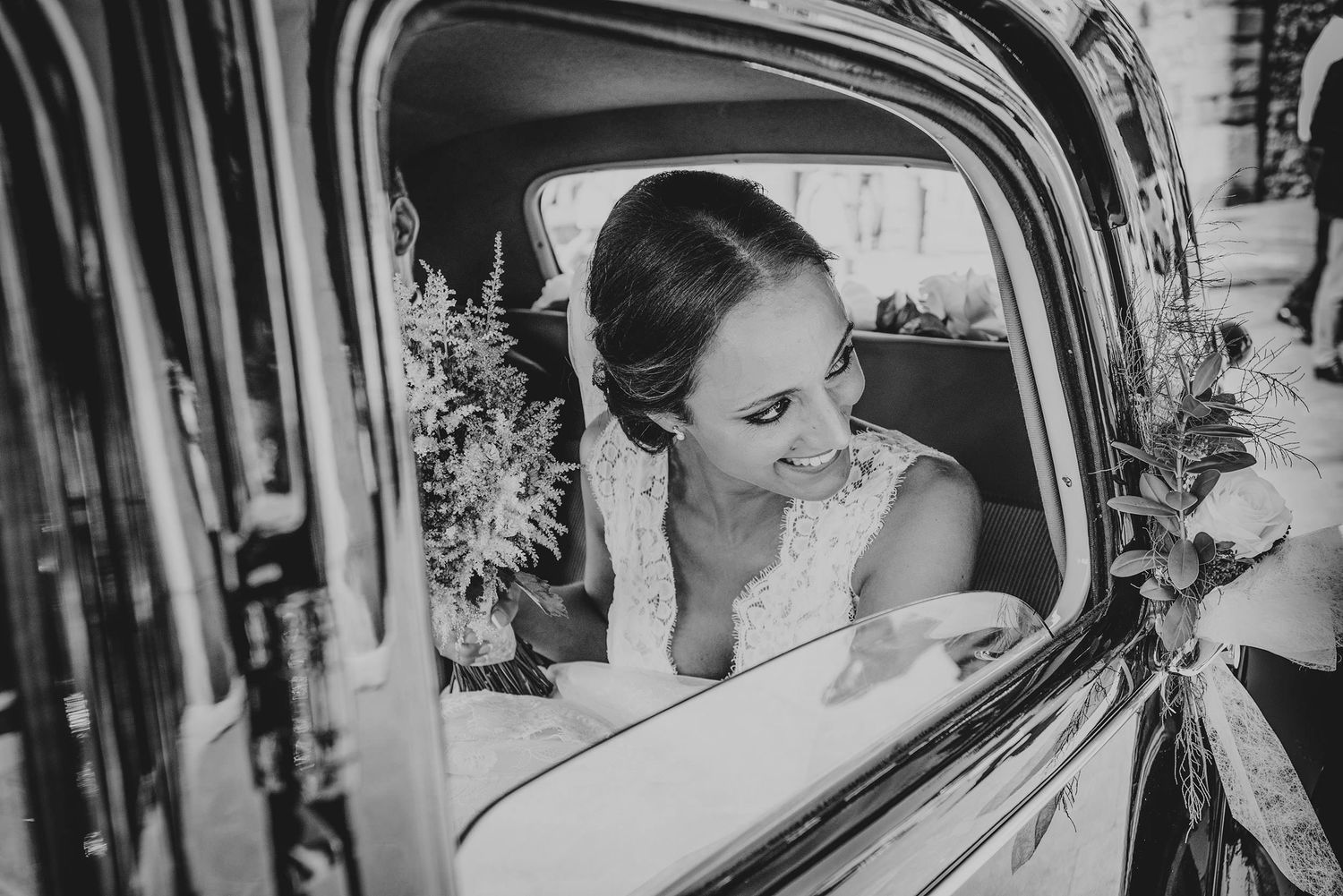 Novia en el interior de un coche clásico justo antes de llegar a la ceremonia de su boda en Asturias, sonriendo mientras sostiene su ramo.