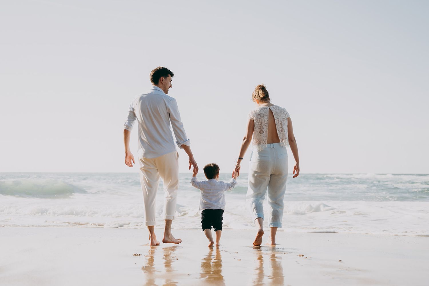 Familia caminando descalza por la orilla del mar durante una sesión de preboda en Asturias, en un momento natural y sin poses