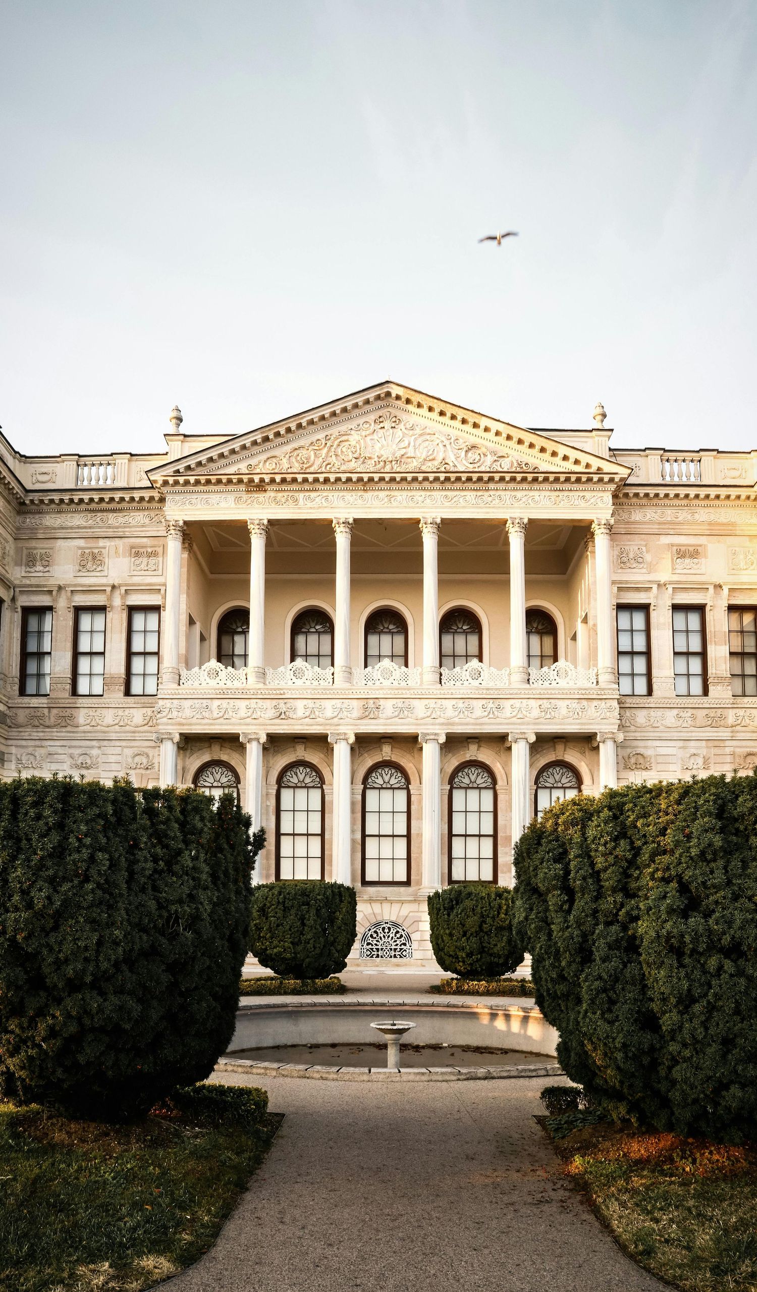 Panoramic view of a grand neoclassical mansion with symmetrical columns and manicured hedges in front of the entrance.