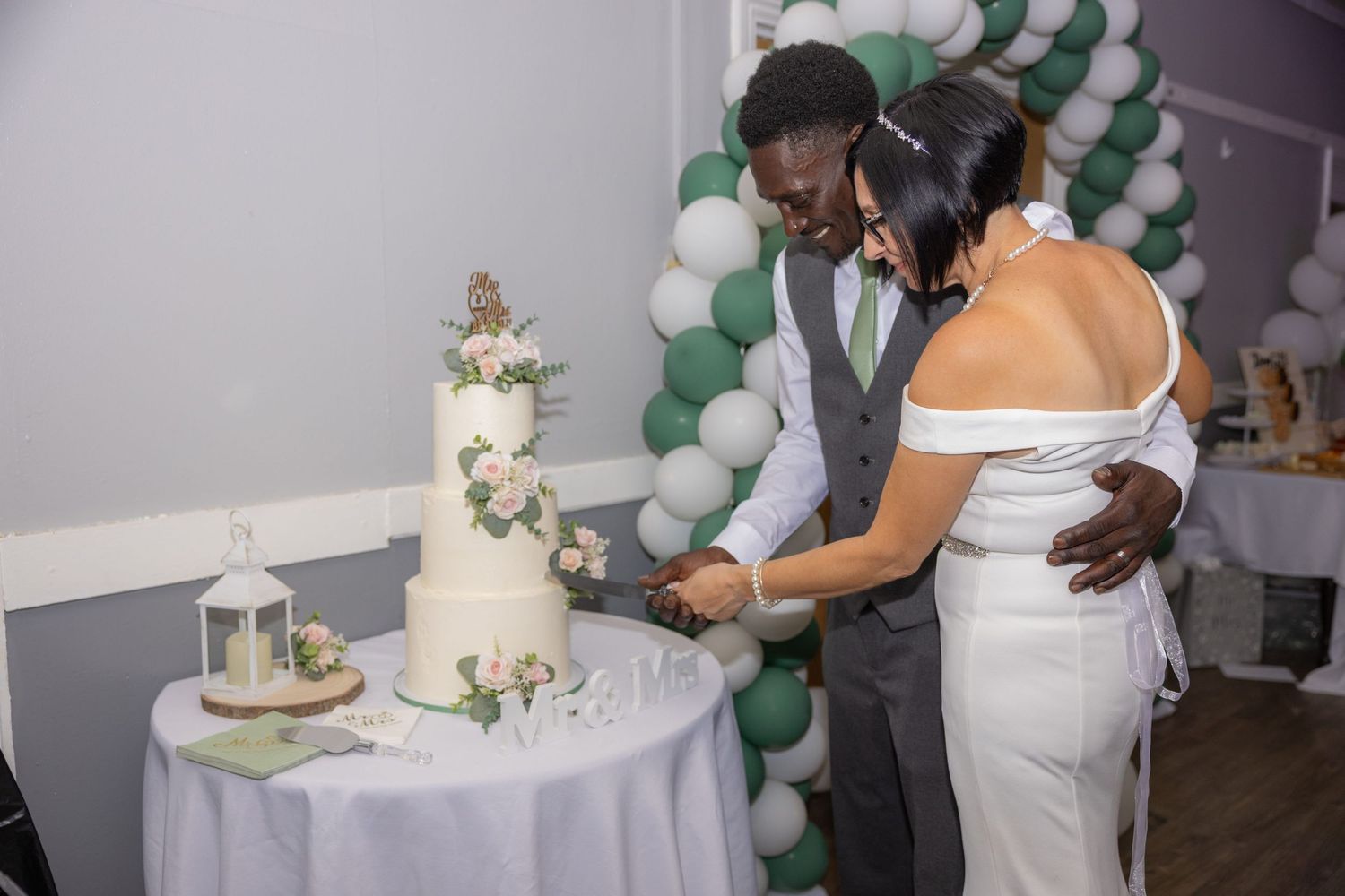 Newlywed couple cutting their white floral wedding cake at their reception.