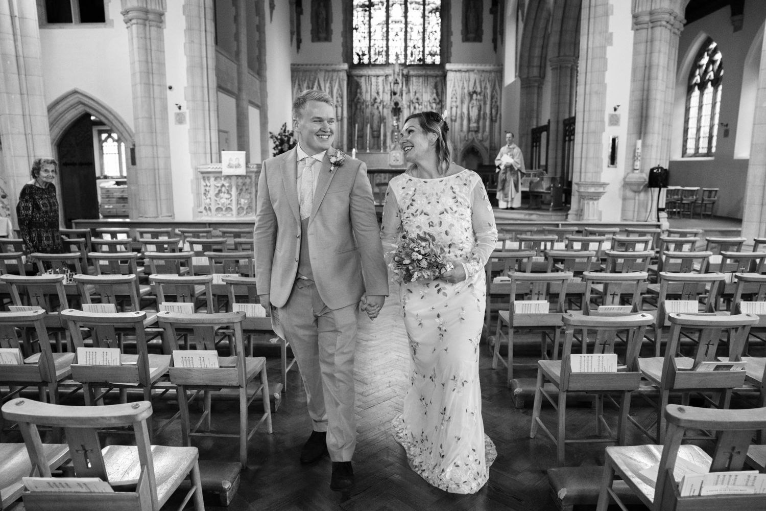 Black and white photo of a bride and groom walking down the aisle of a church after their wedding ceremony.