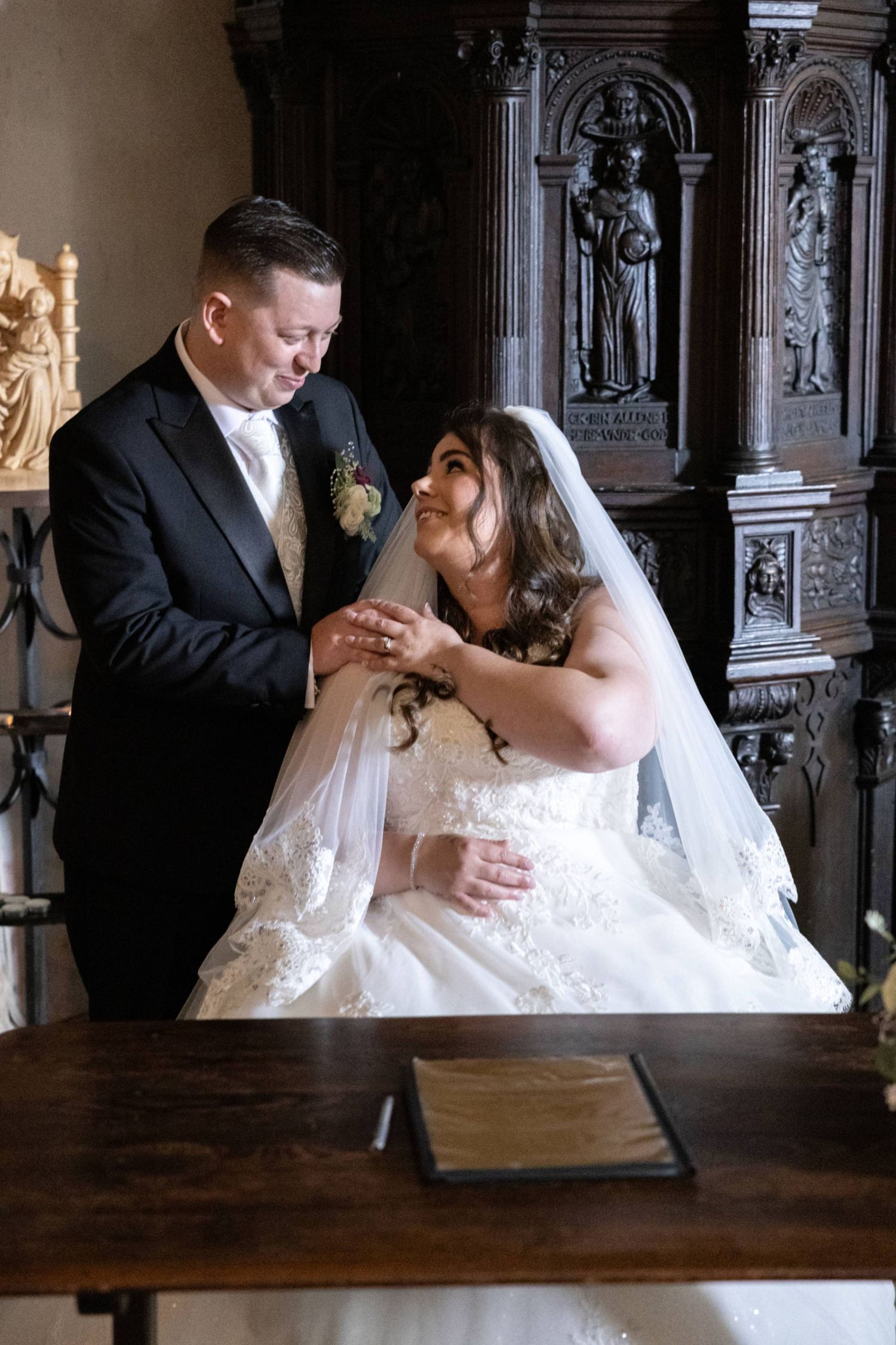 A groom places a ring on his bride's finger during a wedding ceremony in an ornate church setting.