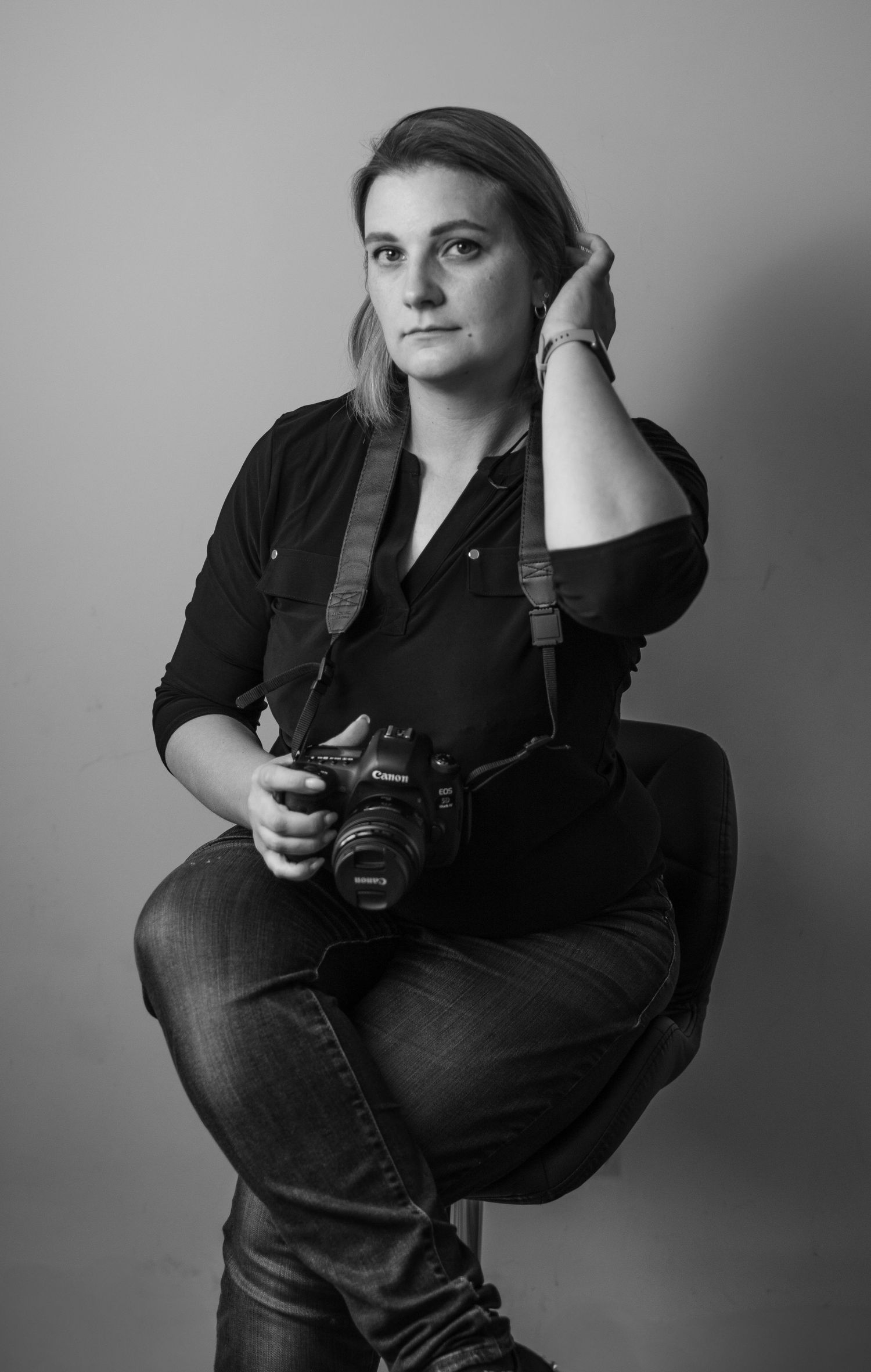 Black and white portrait of a photographer in dark clothing holding a DSLR camera against a plain background.