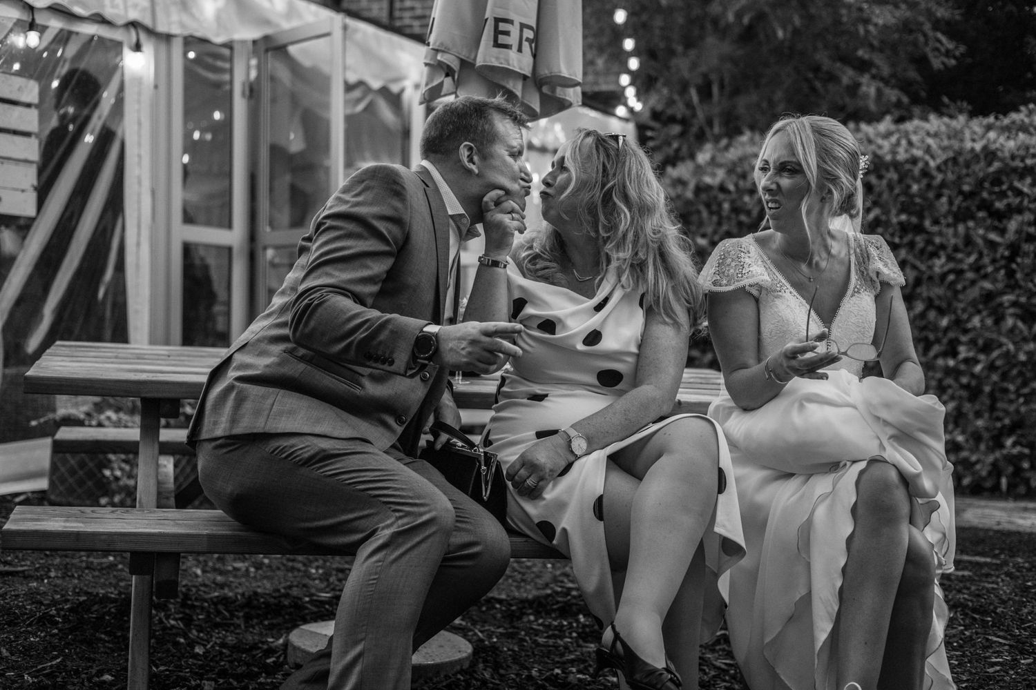 Bride and groom share a moment with a guest at an outdoor wedding reception.