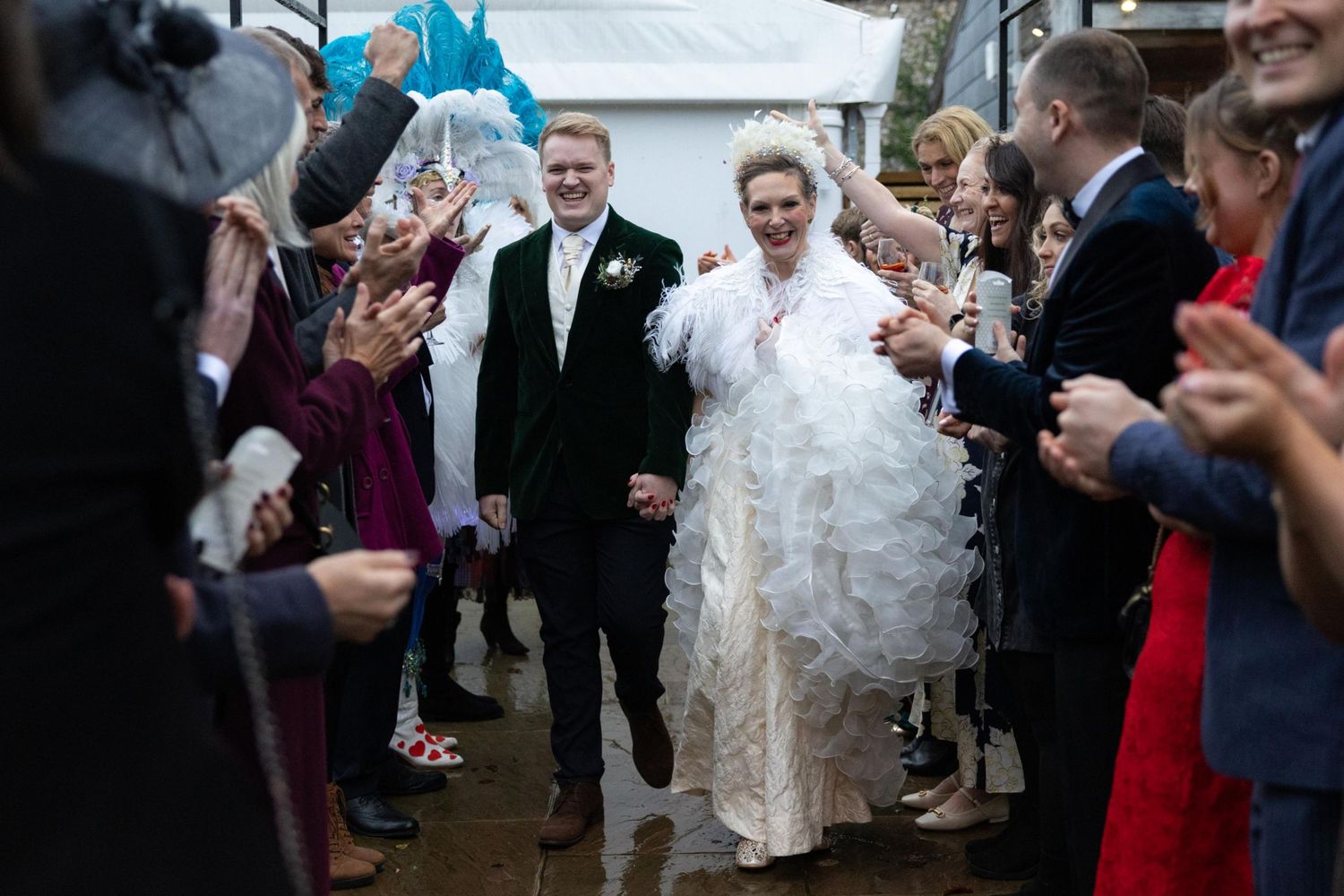 Bride and groom walk through cheering wedding guests throwing confetti outdoors at elegant celebration.
