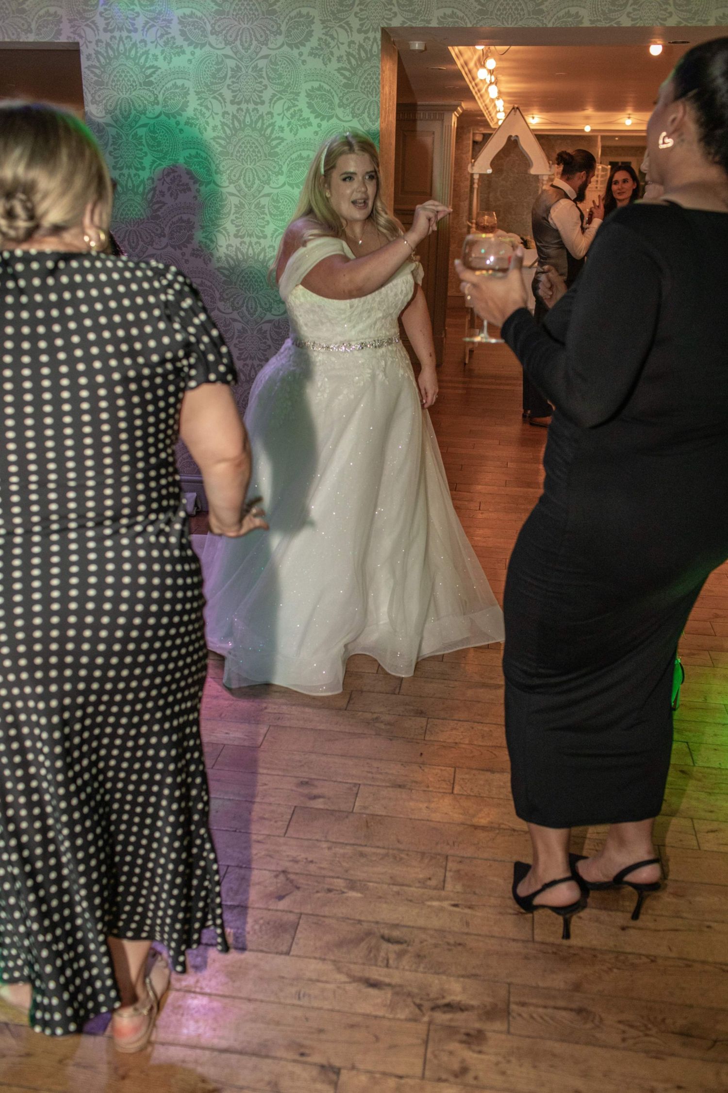 Bride in white gown dancing joyfully with guests on wedding reception dance floor.