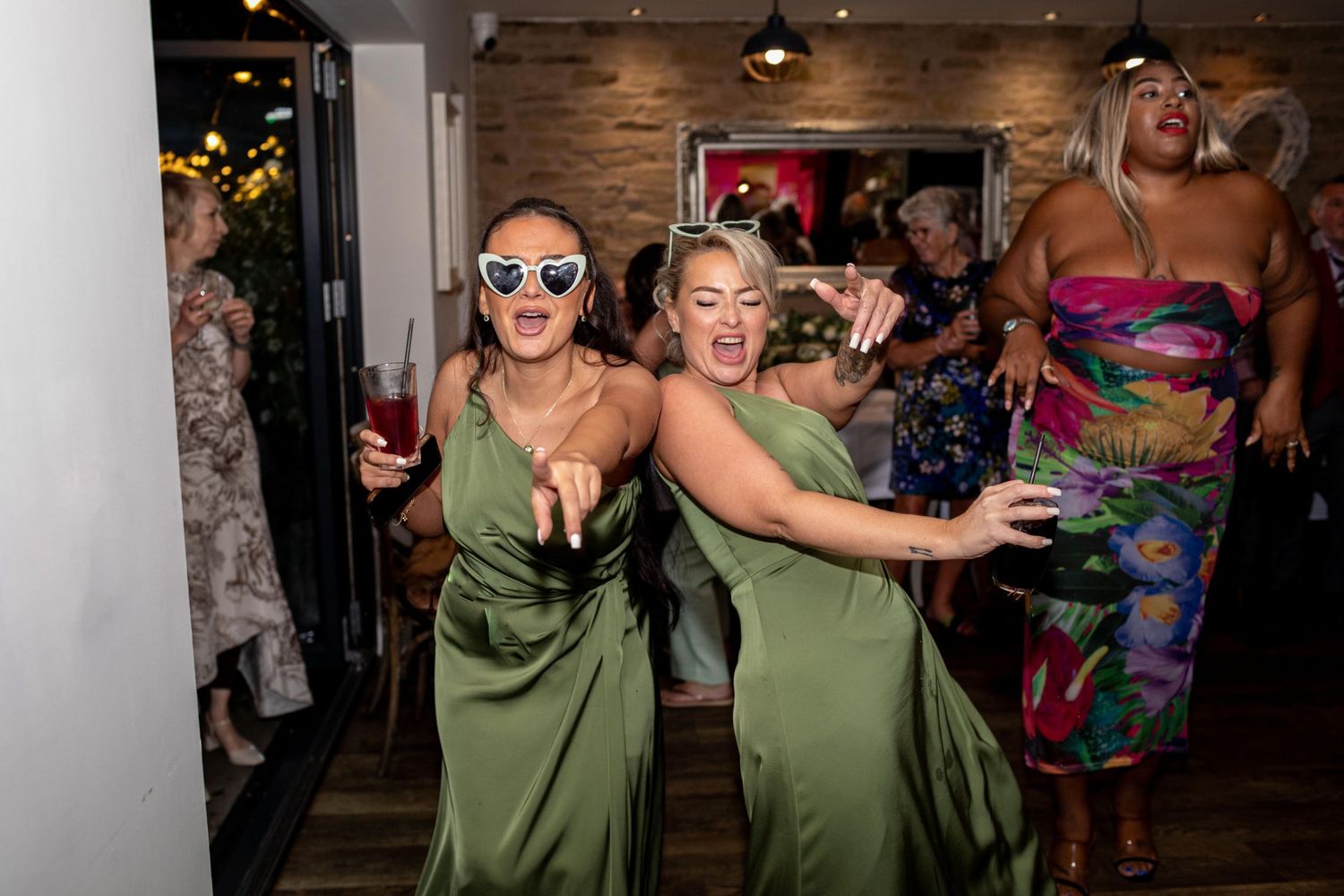 Two bridesmaids in green satin dresses dancing joyfully at a wedding reception party.