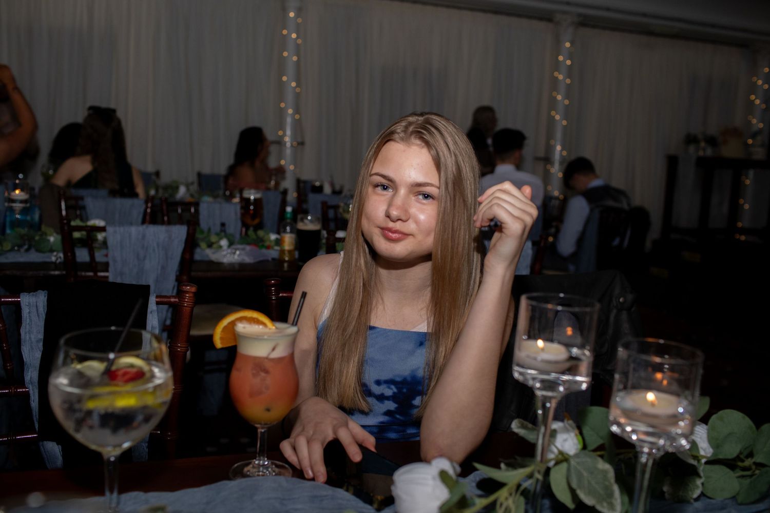 Young woman sitting at an elegantly decorated event table with cocktails and candles in a white tent venue.