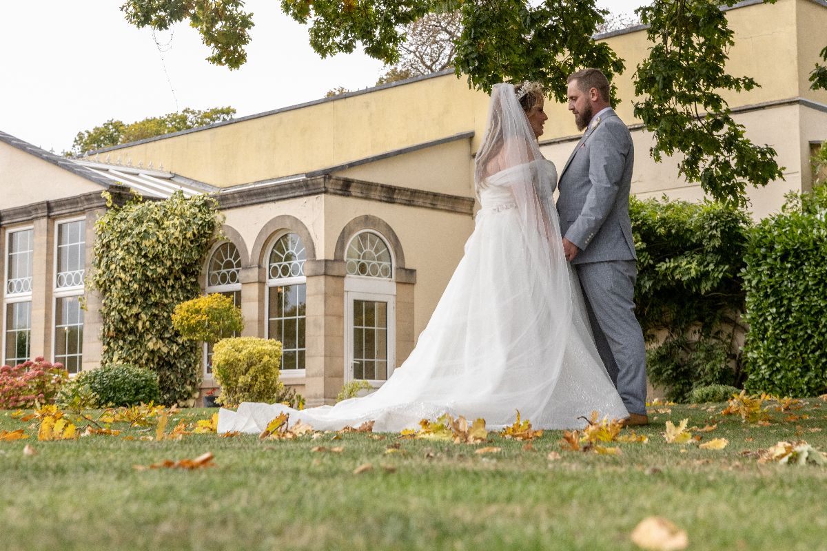 Bride and groom stand together on lush green lawn before elegant venue with arched windows on their wedding day.