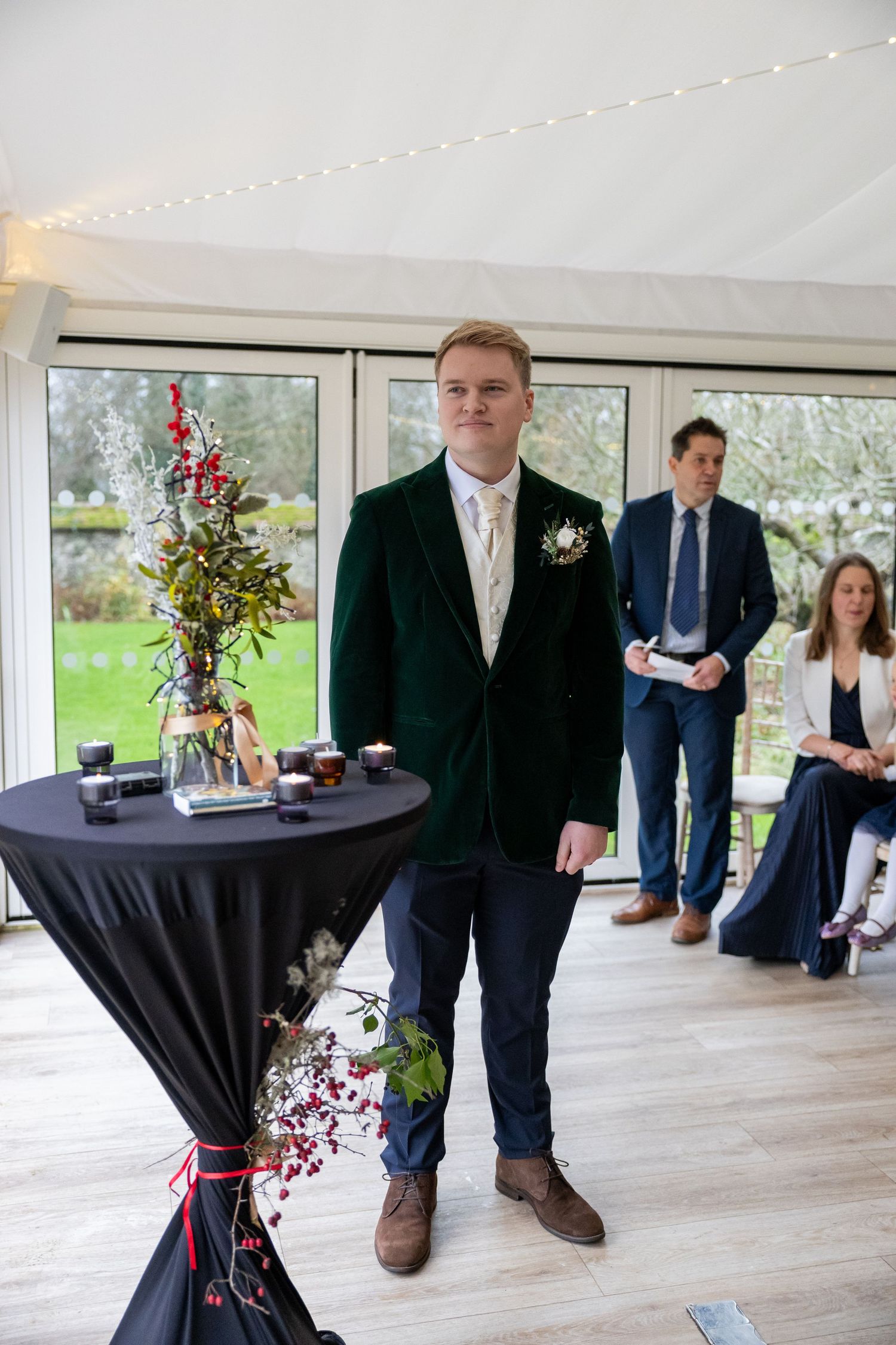 People in formal attire stand near cocktail tables decorated with black tablecloths and floral arrangements at an event.
