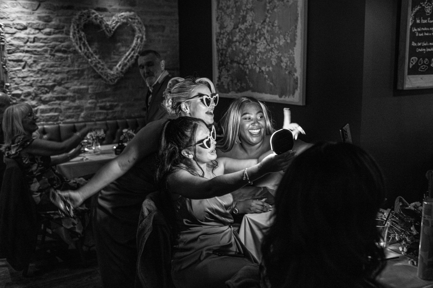 Black and white photo of bridesmaids laughing and taking selfies at a wedding reception.