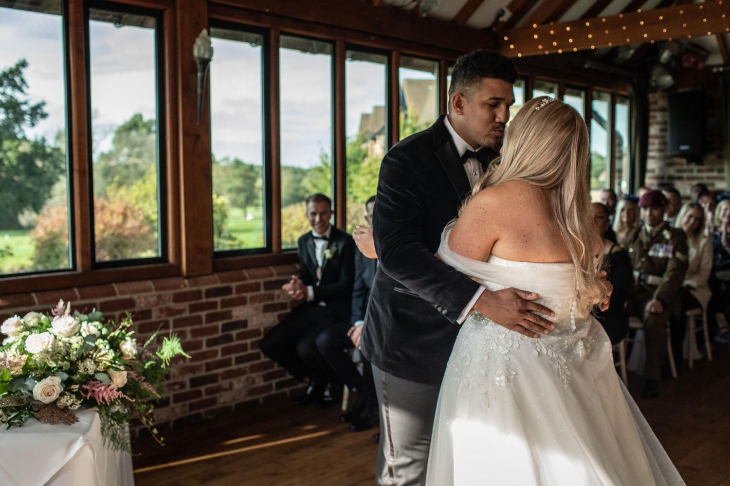 Bride and groom share first dance in elegant venue with brick walls and garden views.