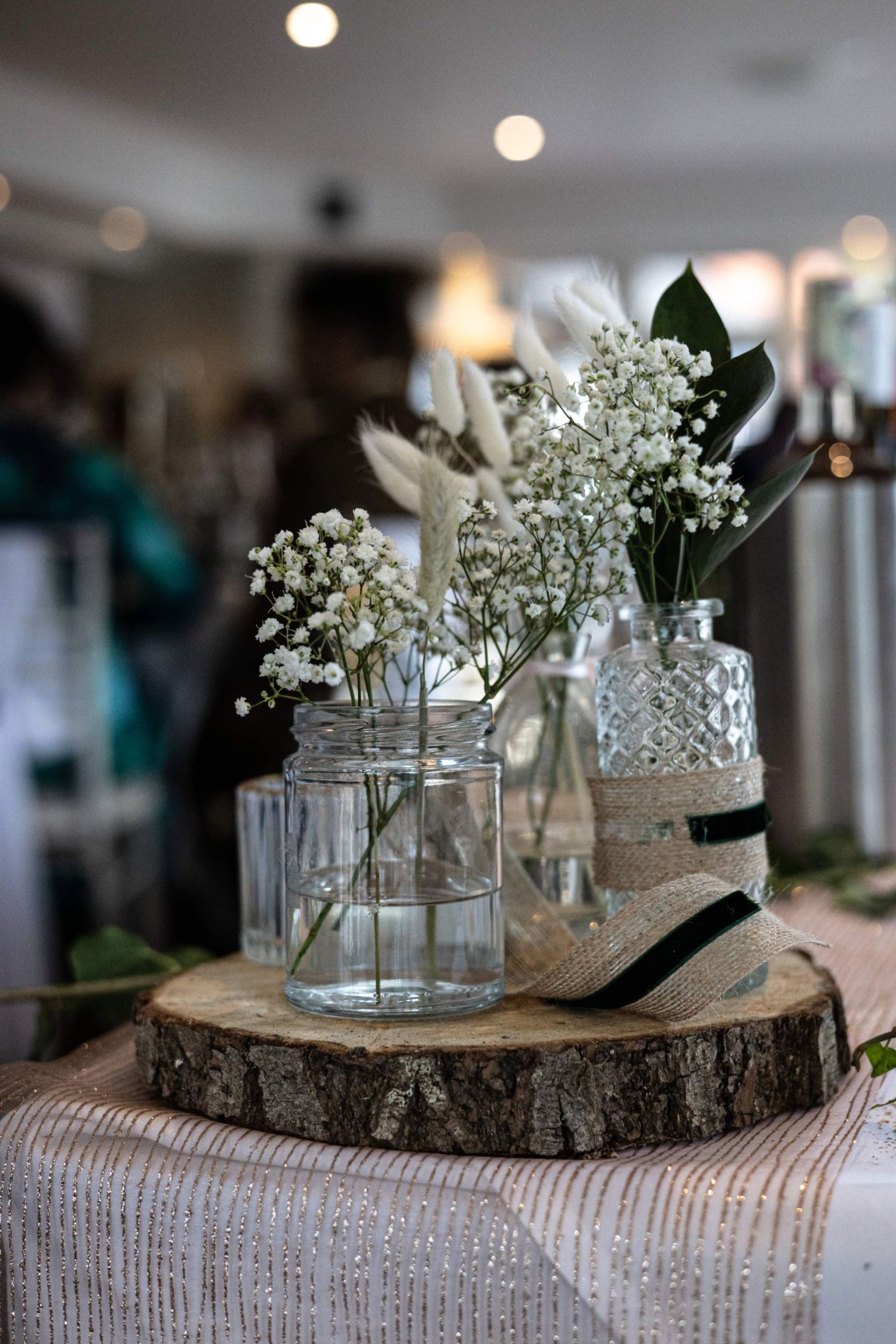Rustic wedding centerpiece with glass vases holding baby's breath and dried flowers on a wood slice with burlap ribbon.