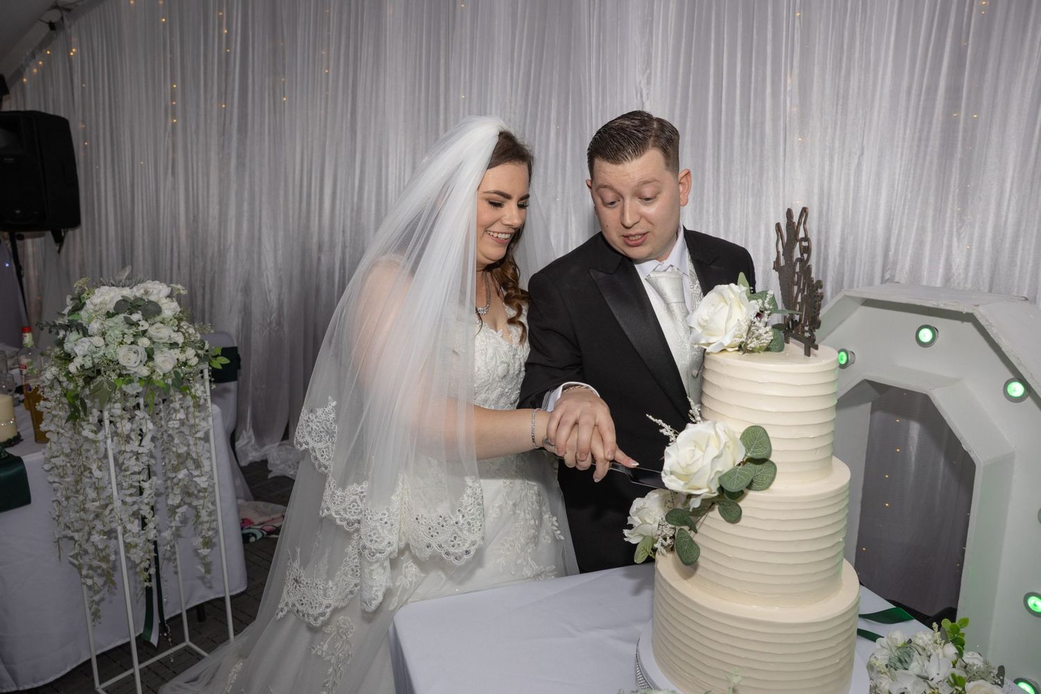 Bride and groom cutting white tiered wedding cake at elegant reception venue.