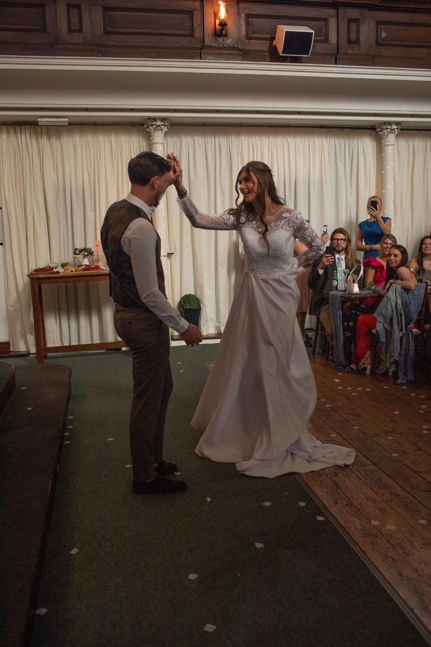 Bride and groom share their first dance at wedding reception, guests watching in elegant wood-paneled venue.