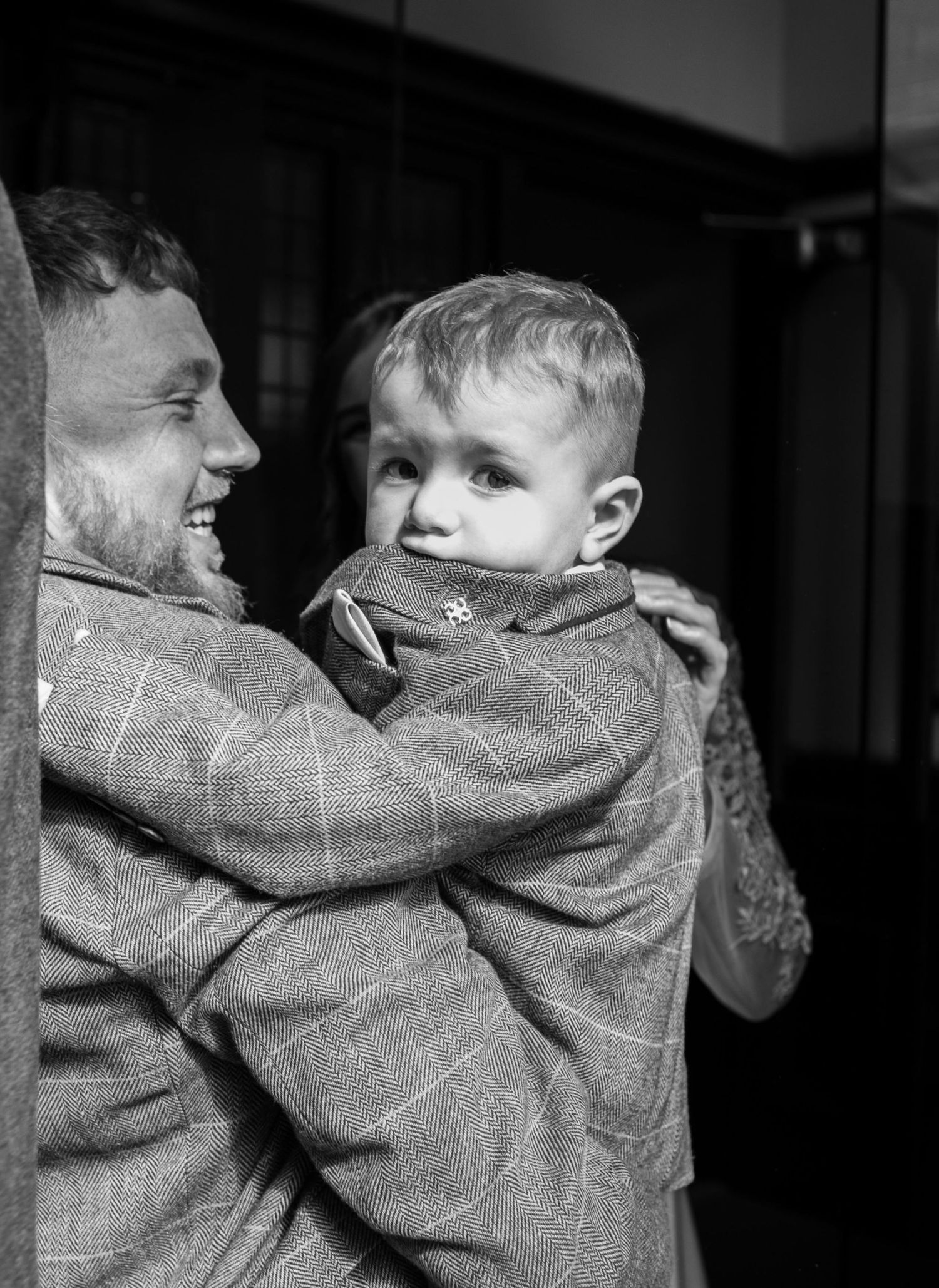 Black and white photo of a smiling man holding a young boy in matching tweed jackets.