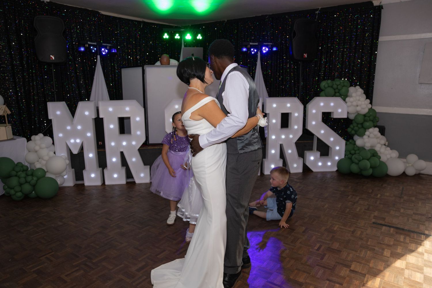 Bride and groom share first dance in front of illuminated MR & MRS letters at elegant wedding reception.