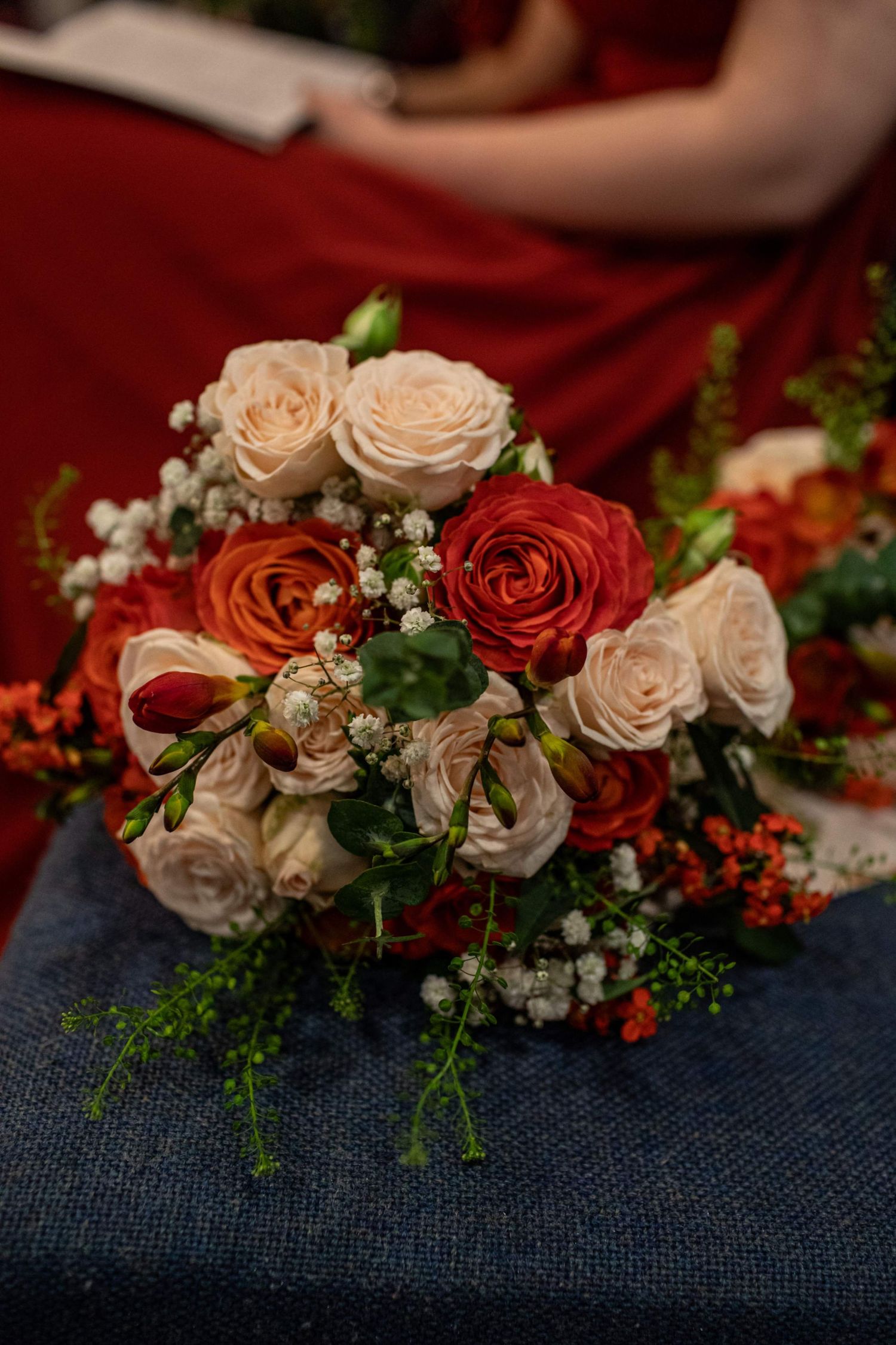 Elegant bridal bouquet with red and cream roses, baby's breath, and greenery on a blue surface.