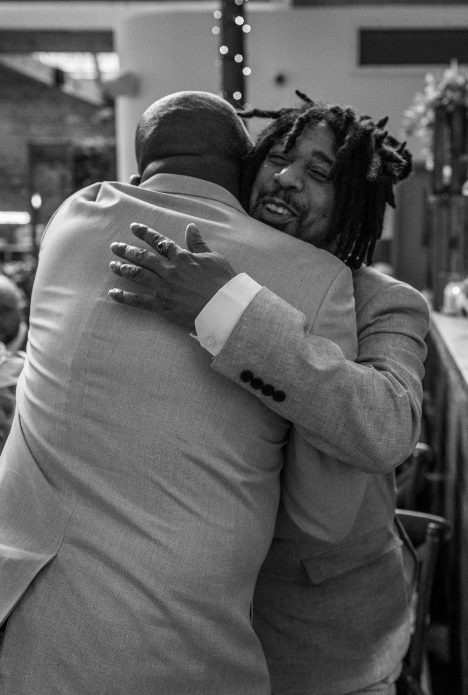 Two men in gray suits sharing a warm embrace at a formal event in a black and white photo.