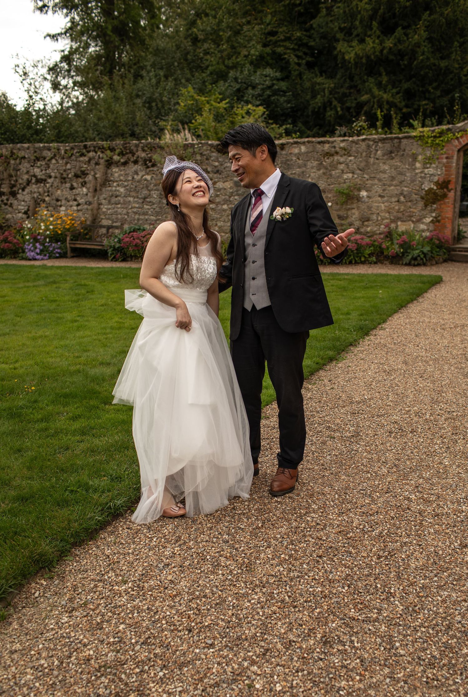 Happy bride and groom walking together in a garden, laughing and smiling on their wedding day.