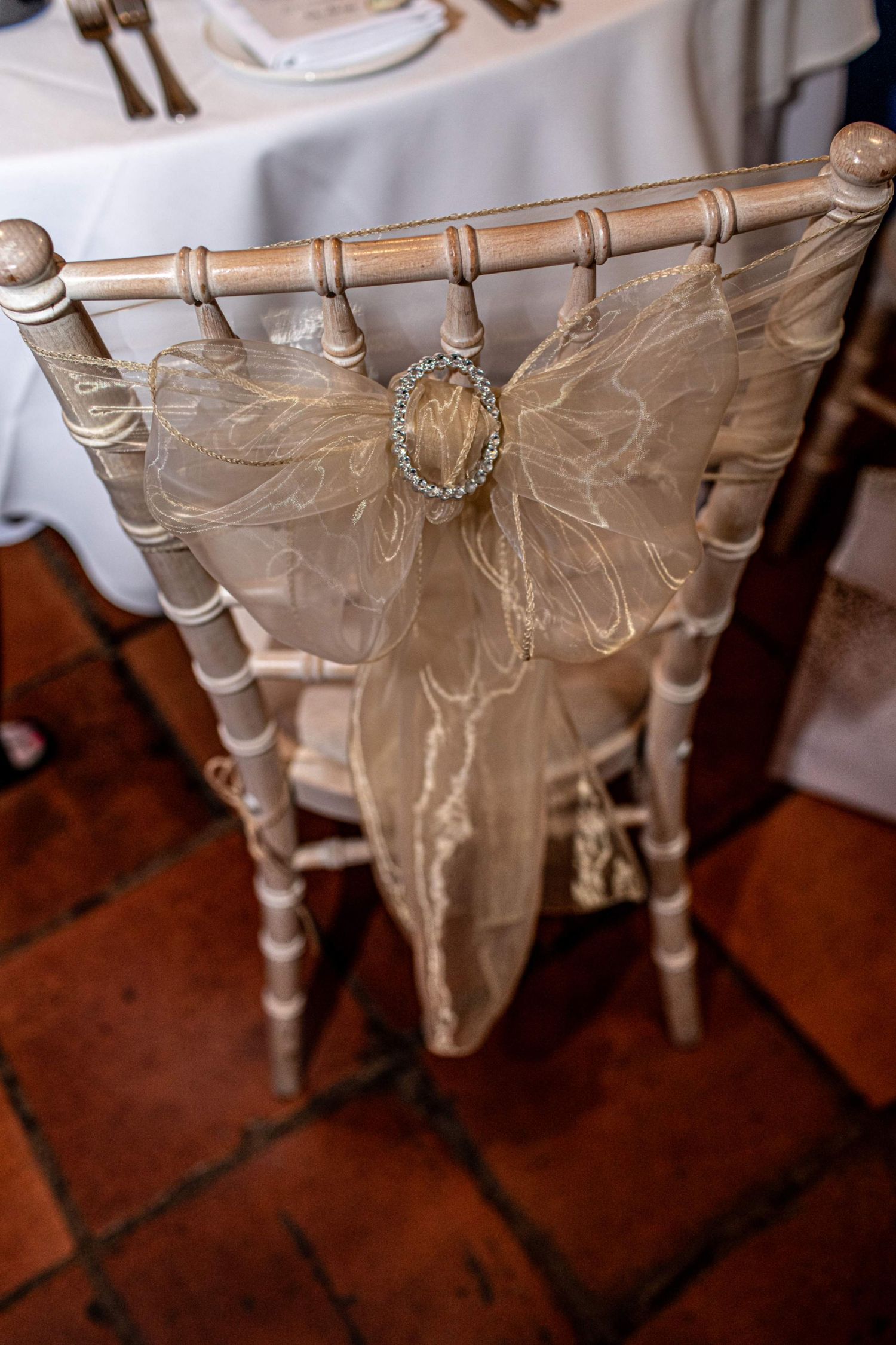 Elegant chiavari chair with champagne organza sash and crystal brooch at a wedding reception.