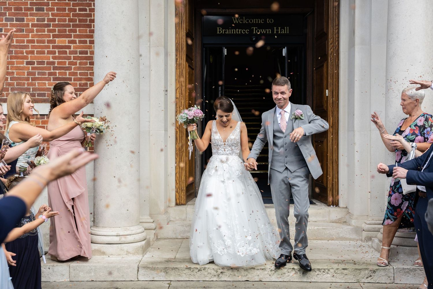 Bride and groom exit wedding venue as guests throw confetti on steps of Braintree Town Hall.