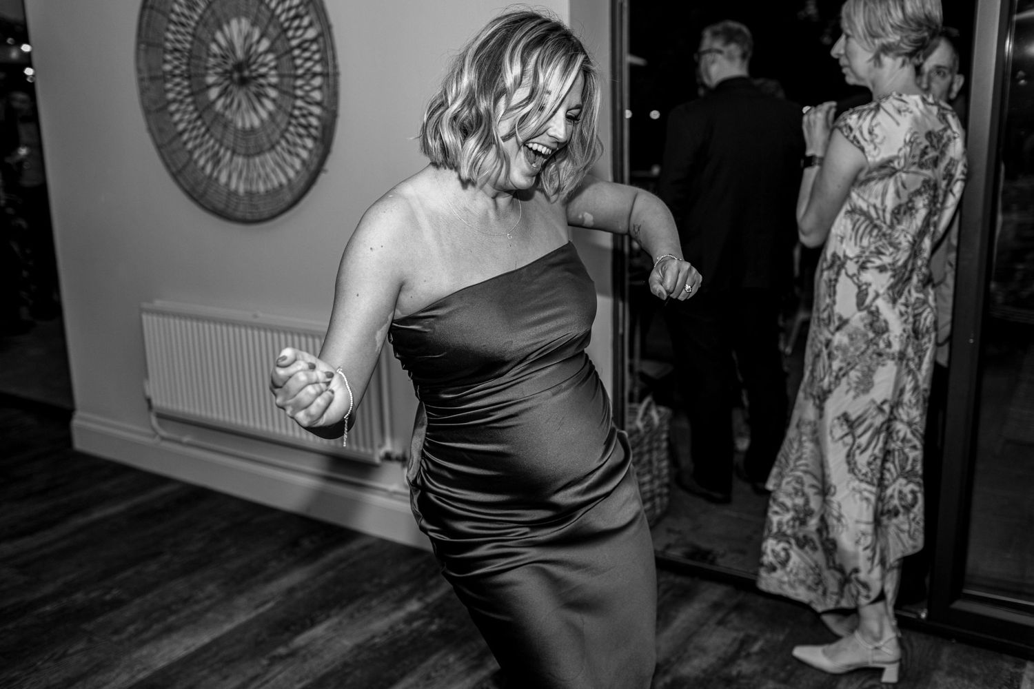 Woman in strapless black satin dress dancing joyfully at an elegant evening event in black and white photo.