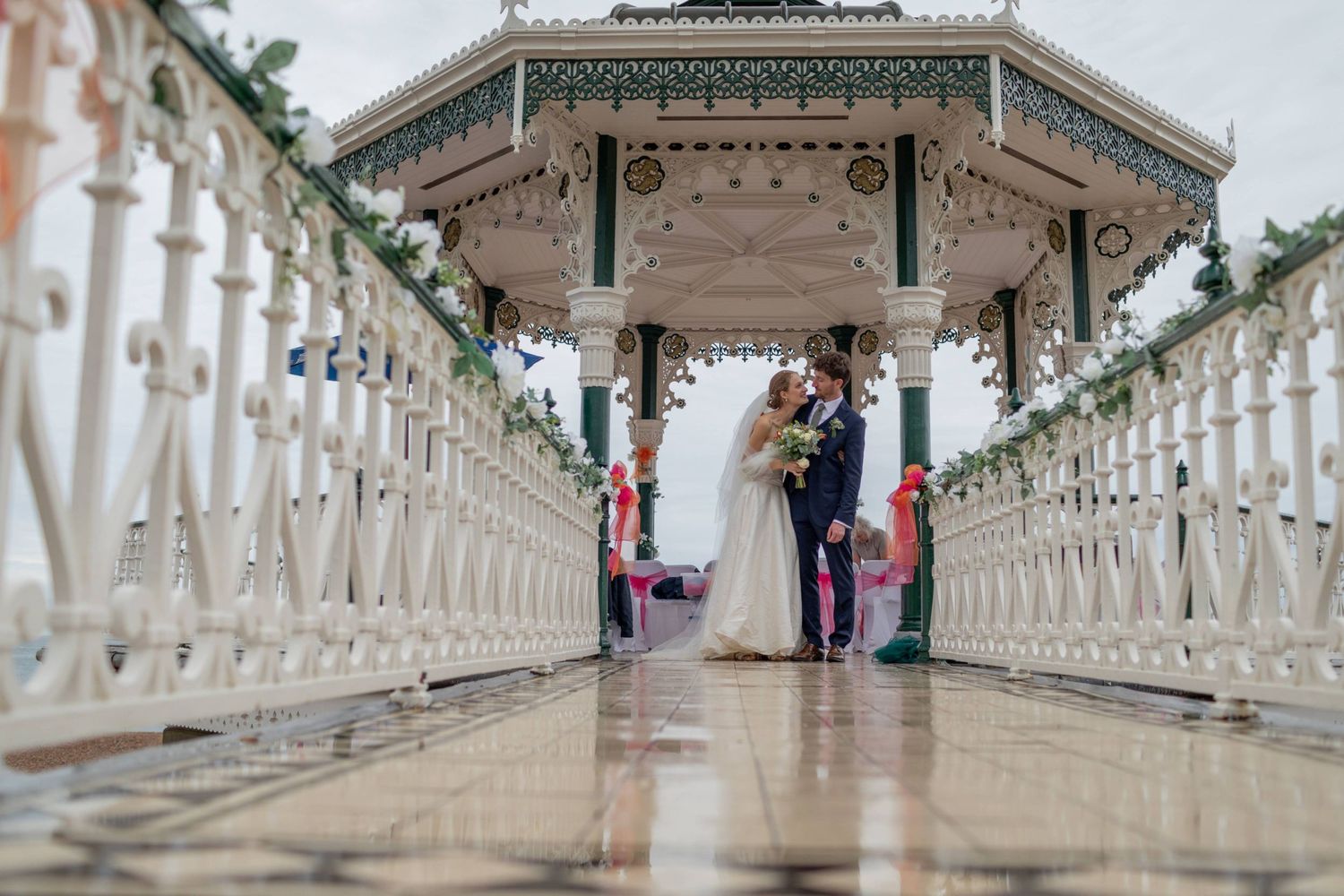 Bride and groom share a kiss at a white Victorian bandstand wedding ceremony with decorative railings.