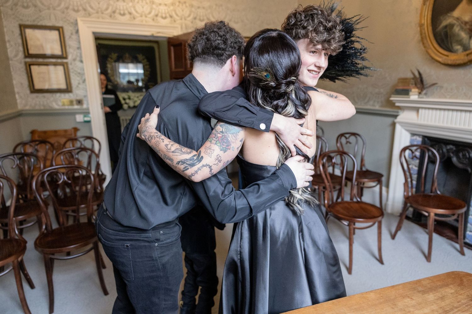 People embrace and comfort each other in an elegant dining room with antique wooden chairs and ornate decor.