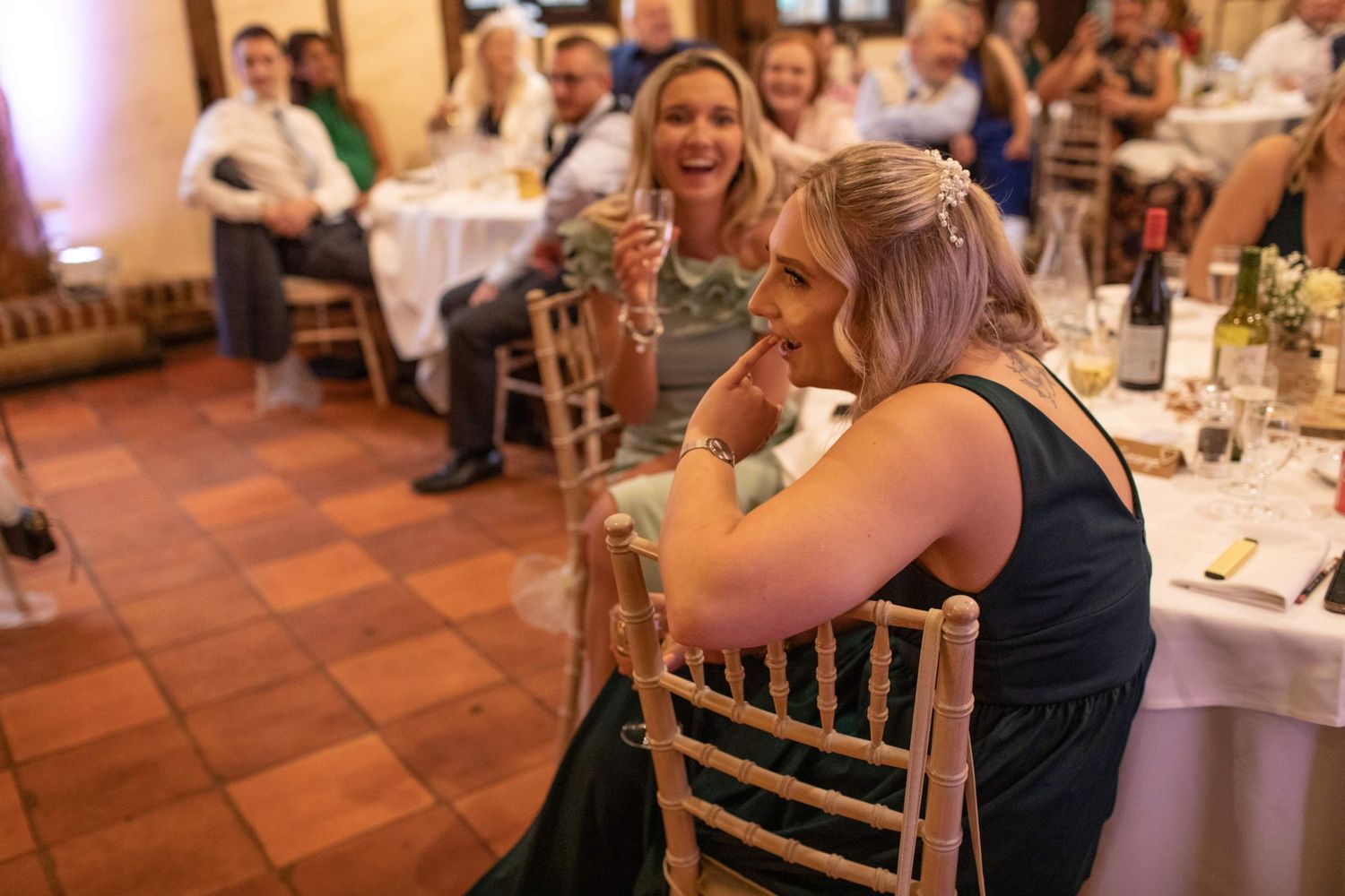 Guests laughing and celebrating at a wedding reception dinner in a warmly lit venue.