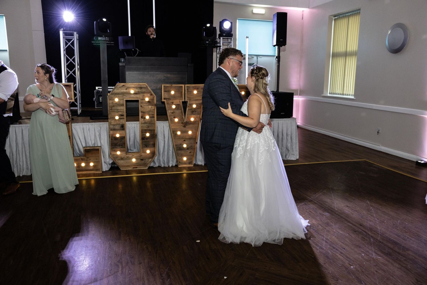 Bride and groom dance together near marquee LOVE letters at bright wedding venue reception hall.