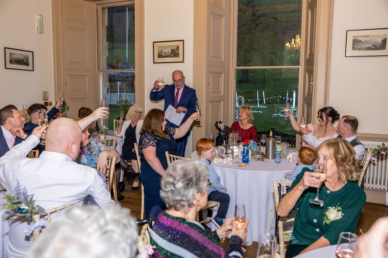 Guests raising glasses in a toast during an elegant wedding reception dinner in a grand venue.