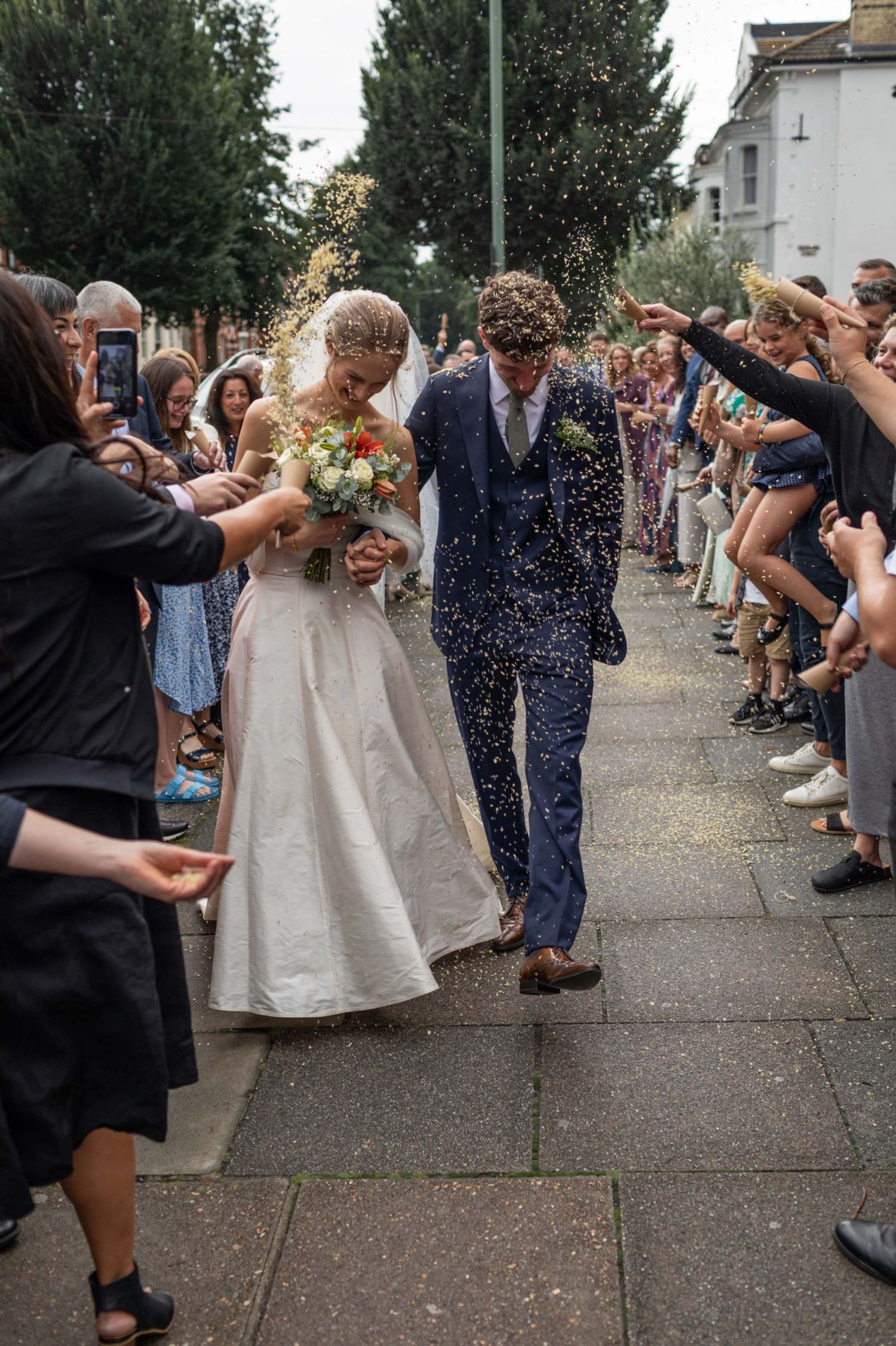 Newlyweds walk through confetti shower as guests celebrate outside church after wedding ceremony.