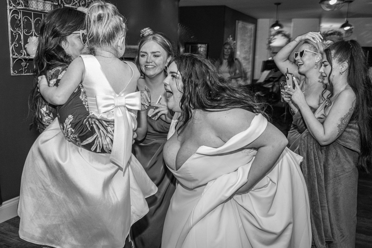 Black and white photo of bridesmaids in dresses joyfully celebrating together at a wedding reception indoors.