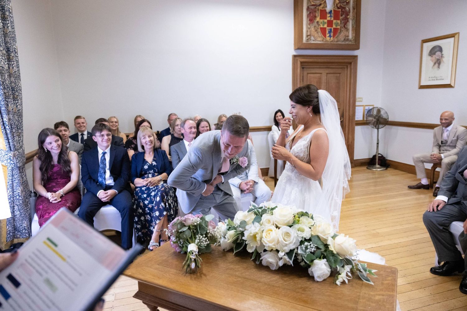 Bride and groom exchange vows at elegant indoor wedding ceremony with white floral arrangements and seated guests.