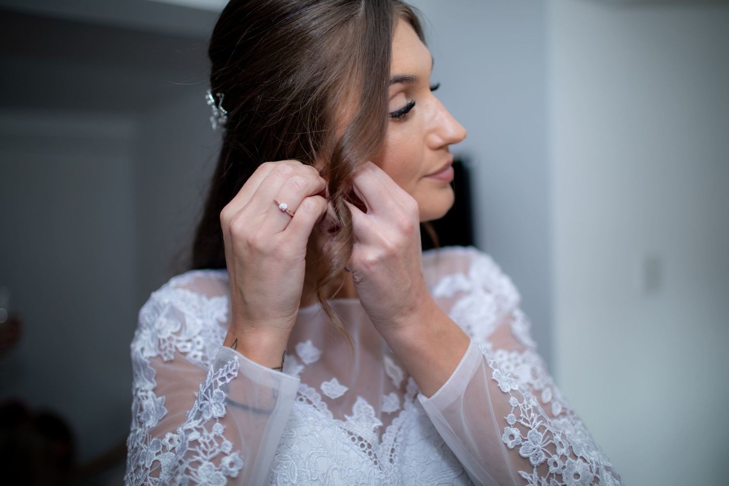 Bride in lace wedding dress putting on earrings while getting ready on her wedding day.