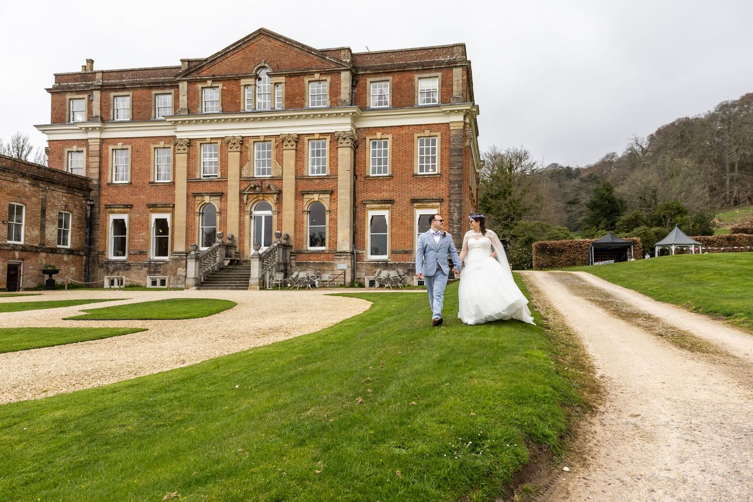 Bride and groom walking hand in hand outside a grand Georgian red brick manor house wedding venue.