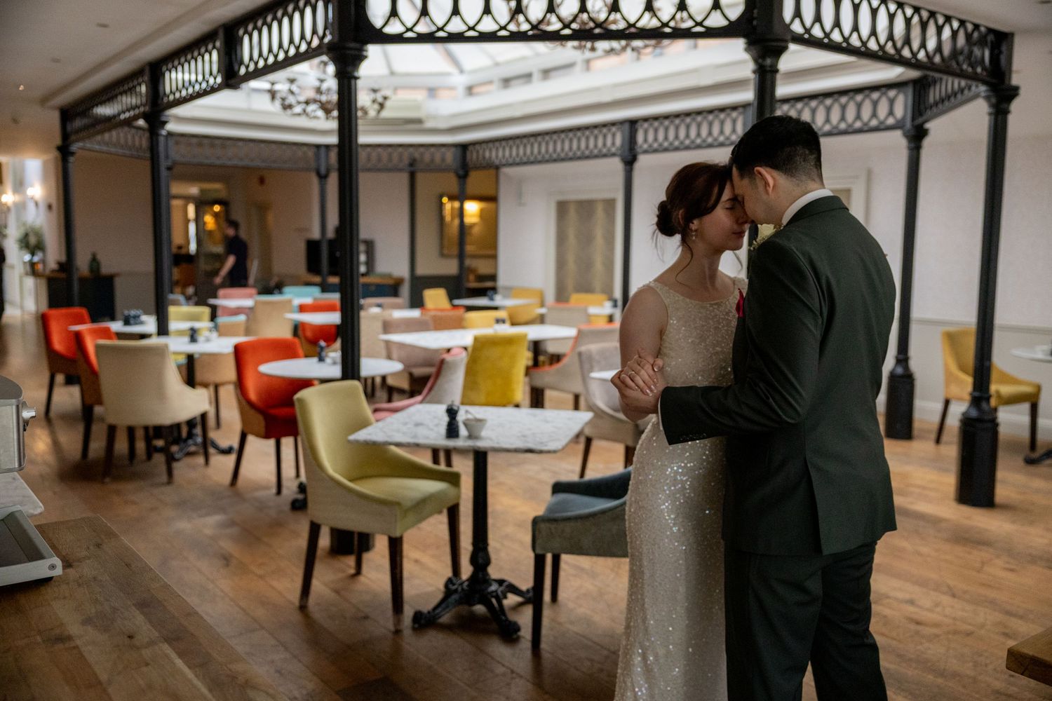 A couple shares an intimate moment in an elegant restaurant with colorful chairs and hardwood floors.
